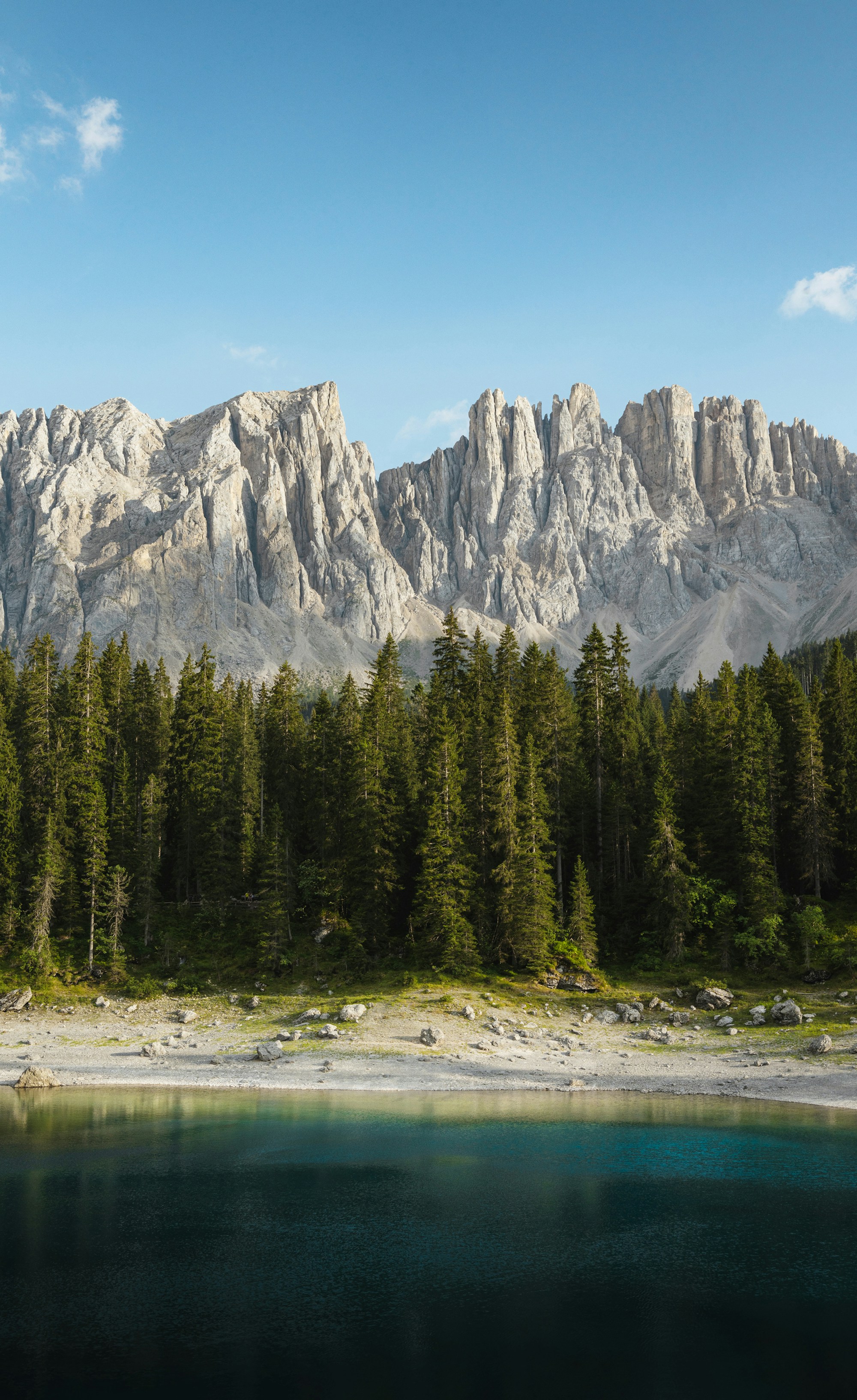 Still alpine lake beneath forested slopes and rocky peaks. Photo by Pierre Jeanneret / Unsplash.