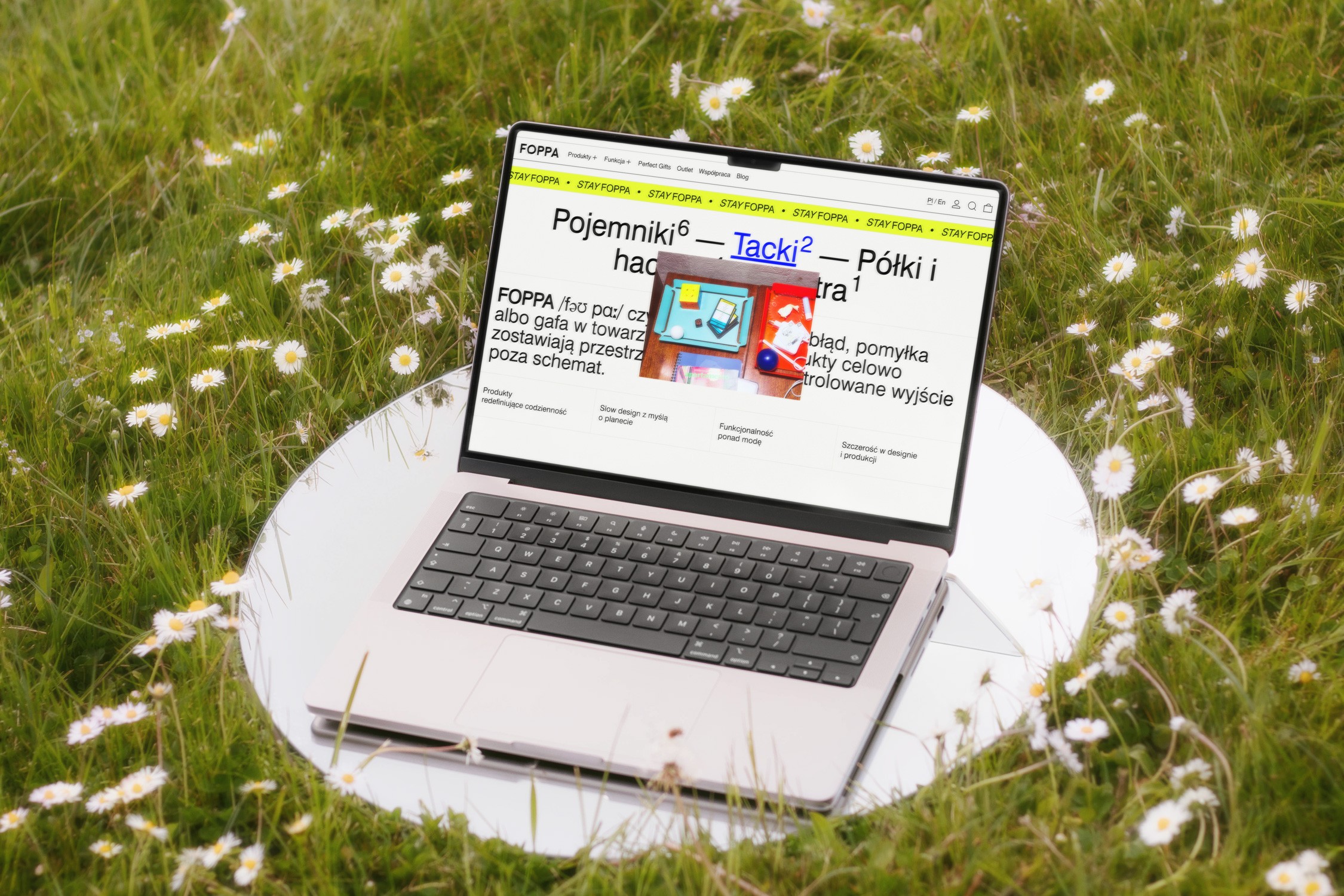 A laptop with a colorful screen sits on a round table in a grassy area adorned with small flowers.