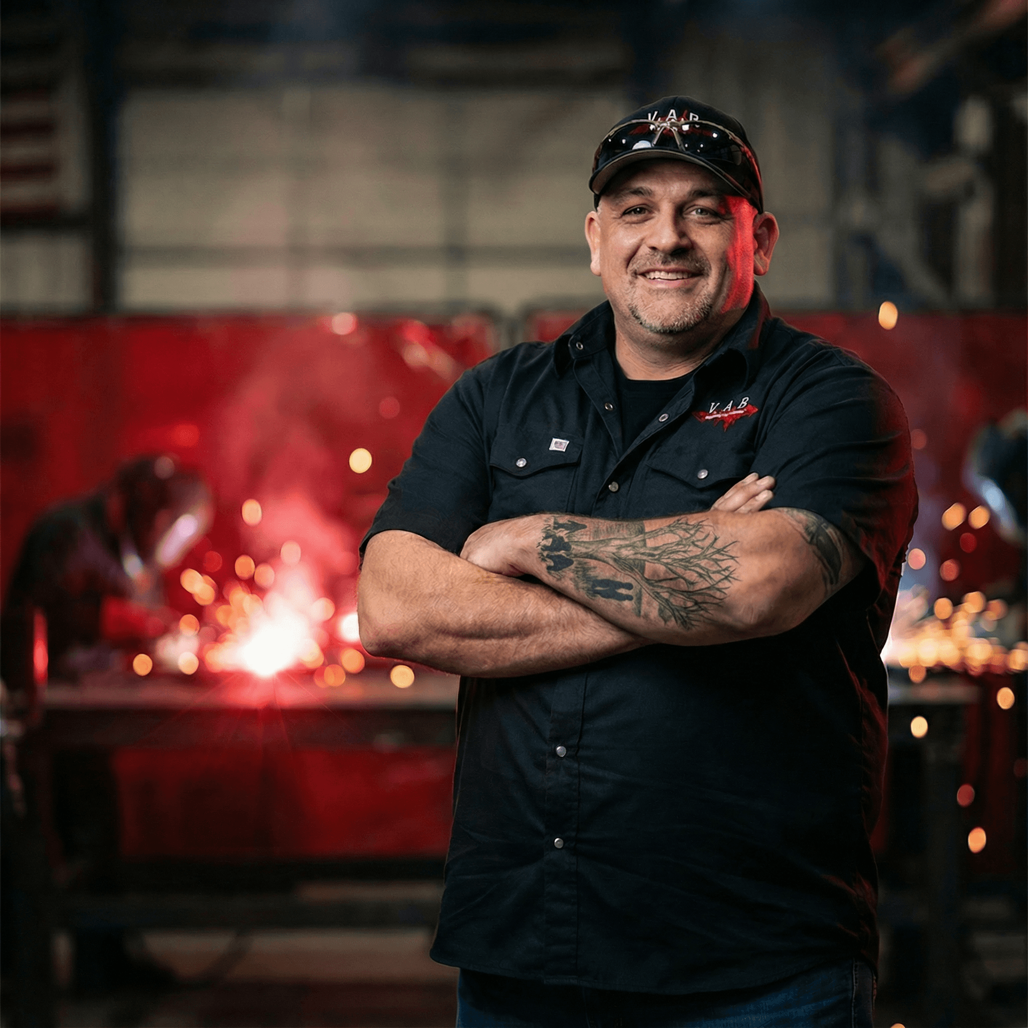 Man with short hair and beard wearing a dark blazer and black shirt against a plain background.