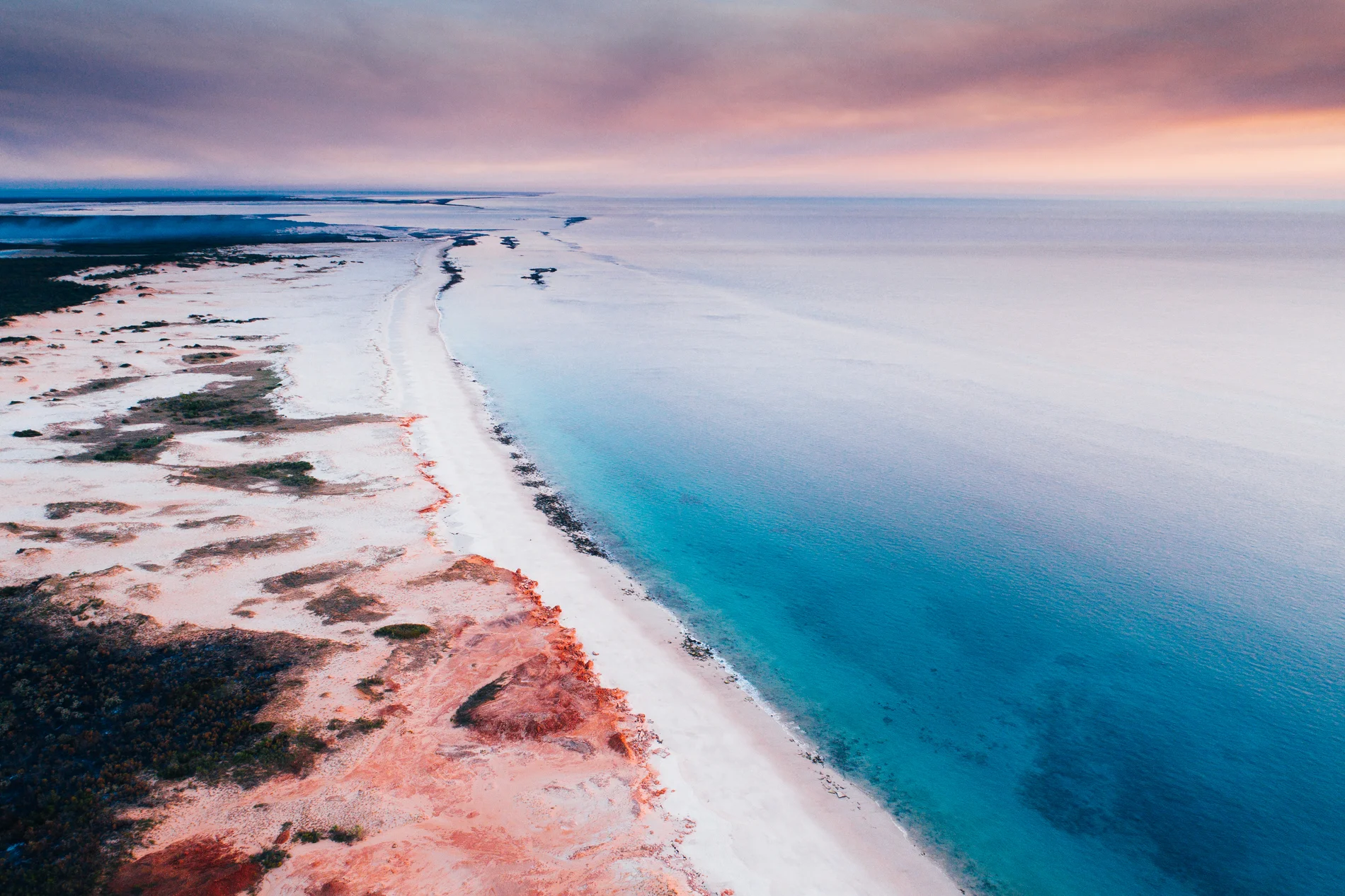 Aerial at dusk of tidal flats and pale sandbars in soft pink light