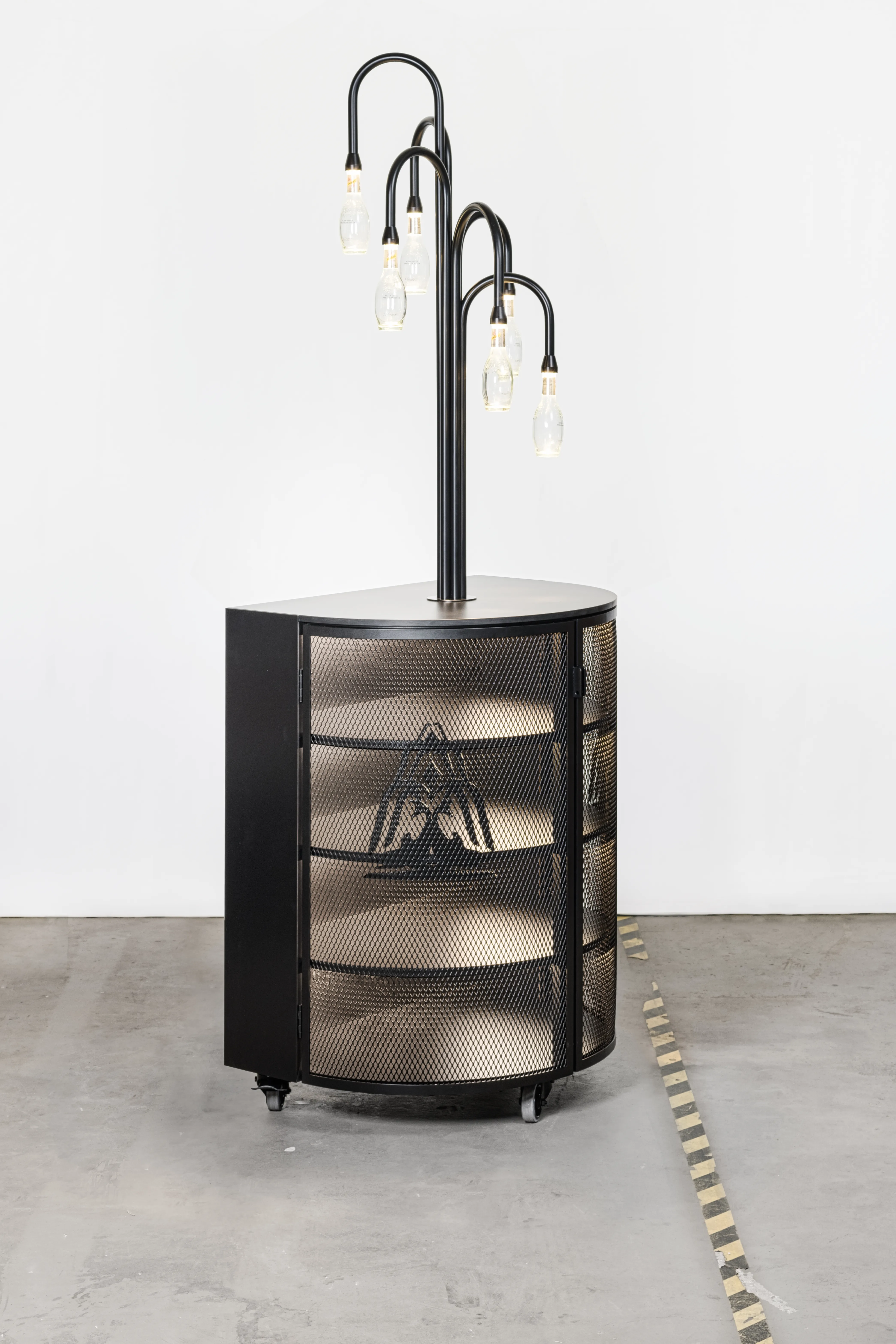 Free-standing SCHWEPPES bar column with rounded perforated metal front, triangle logo cutout and a cluster of bottle lamps on curved black arms.