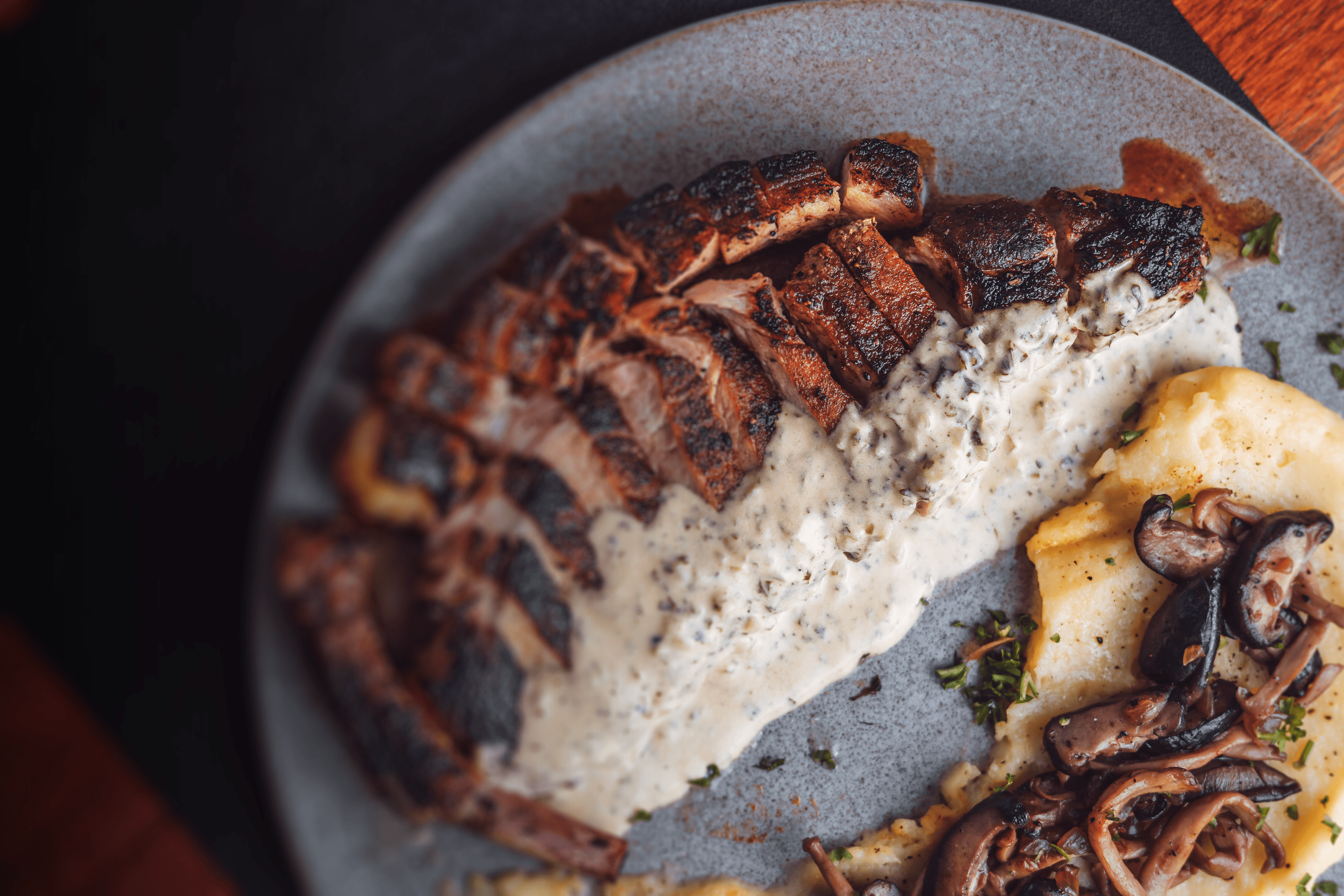 Four pieces of fried chicken or battered fish on a bed of salad greens, being heavily topped with shredded white cheese that is raining down onto the dish, set against a dark, rustic background of wood and pine cones.