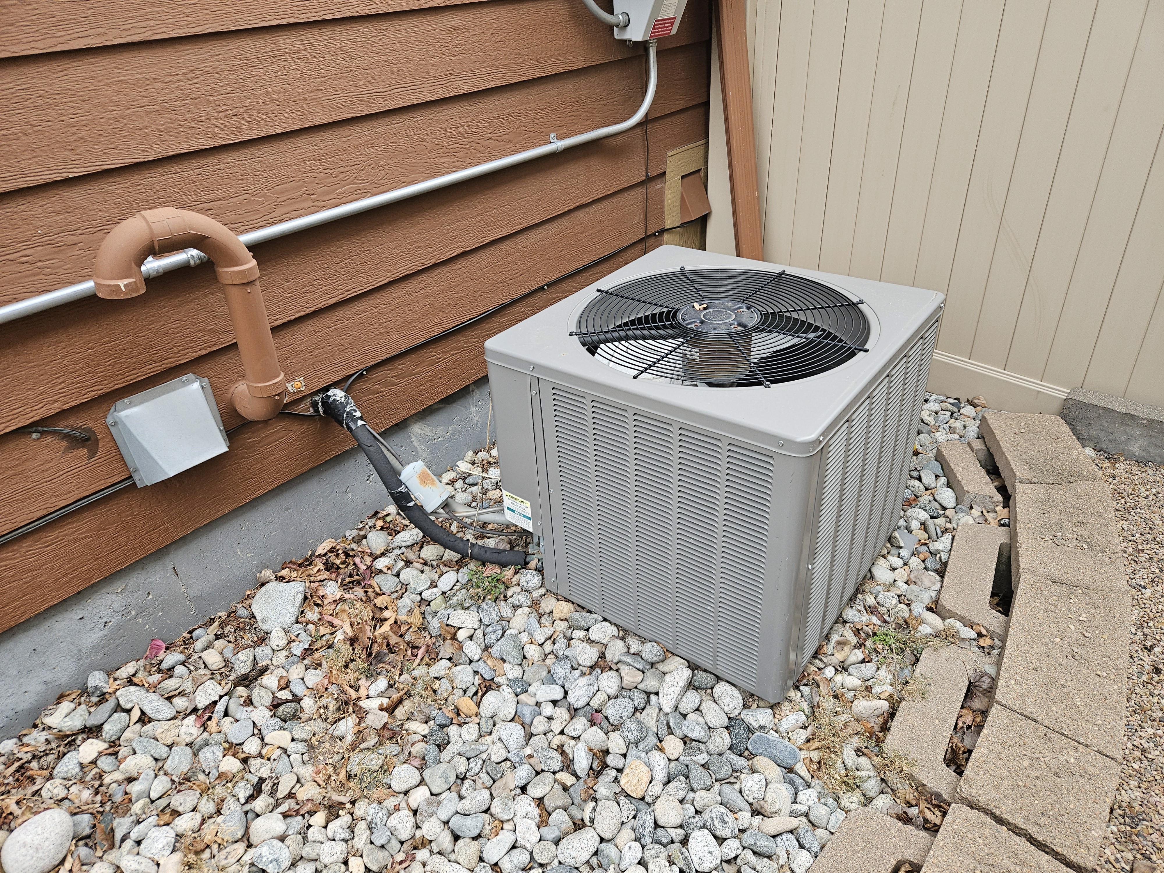 The image shows an outdoor central air conditioning unit, which is part of an HVAC system that removes heat from an enclosed space to provide cooling and humidity control.