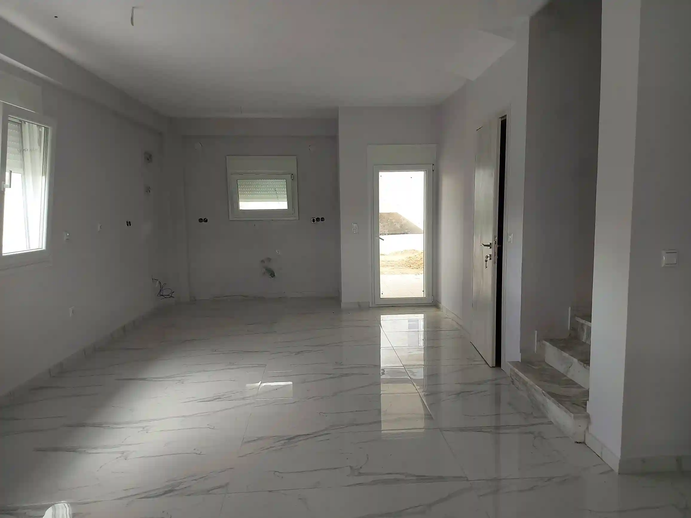 Άδειο μοντέρνο σαλόνι με γυαλιστερό μαρμάρινο δάπεδο, εσωτερική σκάλα και πρόσβαση σε εξωτερικό χώρο.