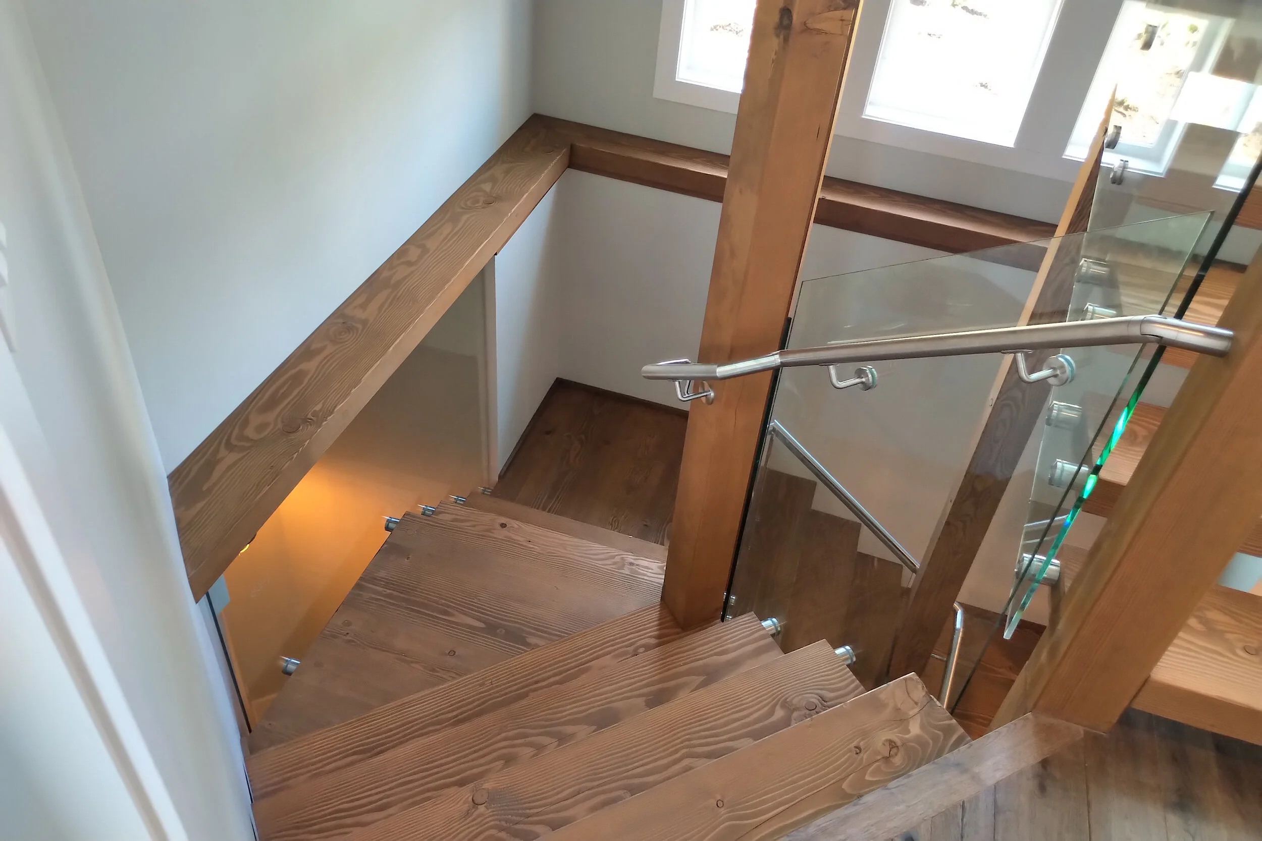 Interior wooden staircase with clear glass railing and brushed metal handrail, enhancing open-concept home design by Tenmar.