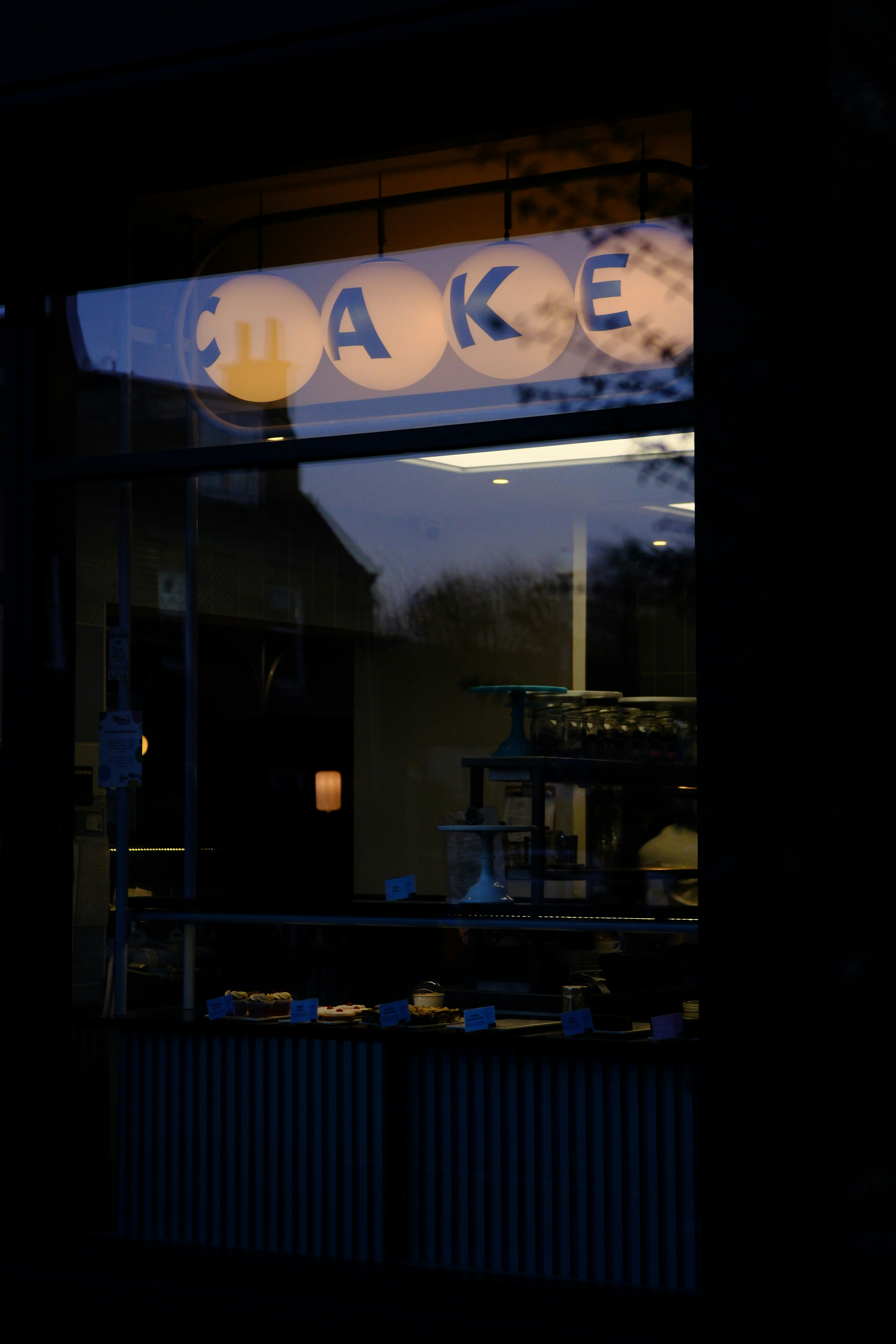 A window with a lit up sign that says cake shop