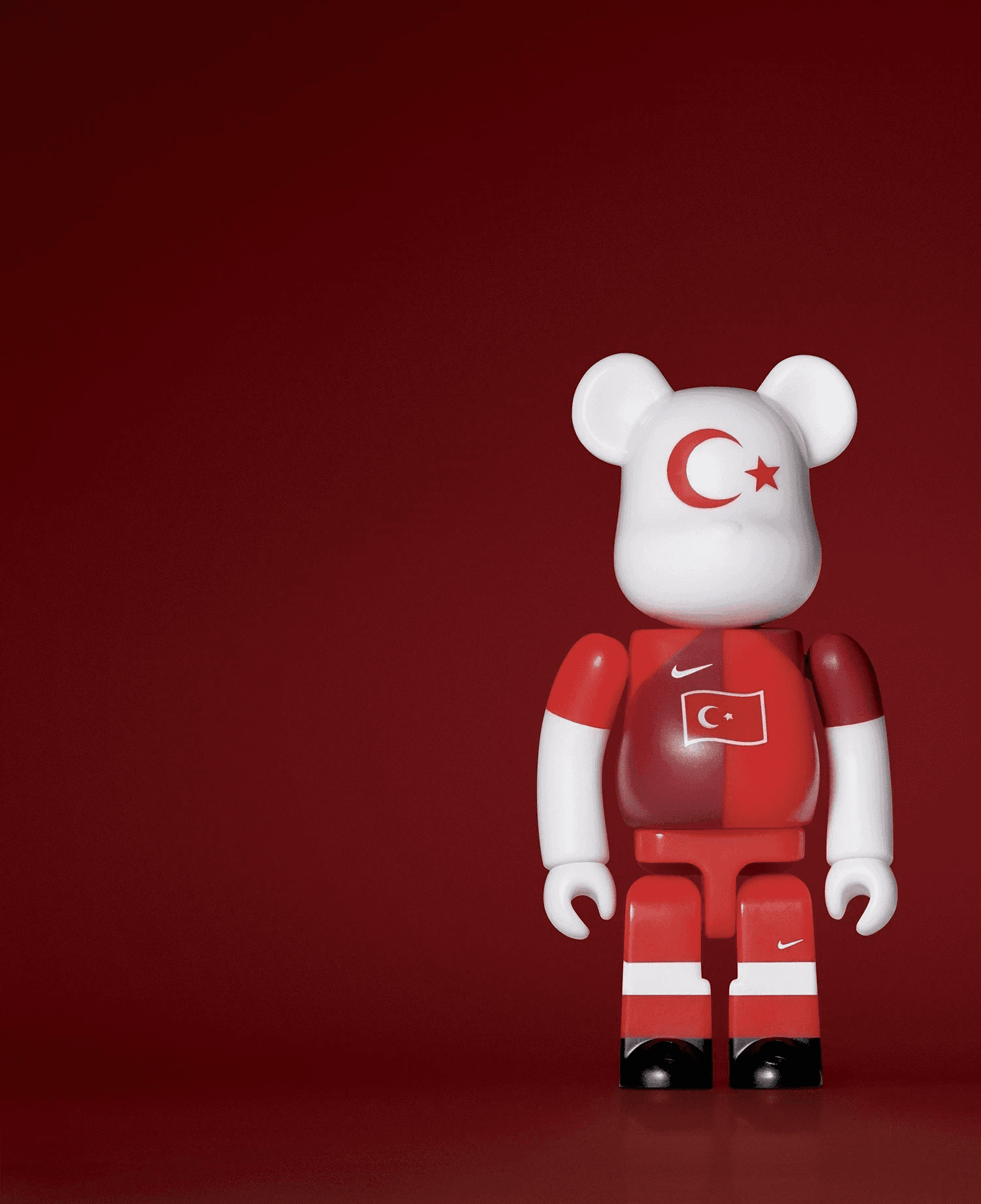 A single 3.5” tall Bre@rbrick/Nike toy created to commemorate the 2006 Turkish World Cup football team. The toy is painted to appear in the Turkish football kit and stands in the center of the frame in front of a dark red background.