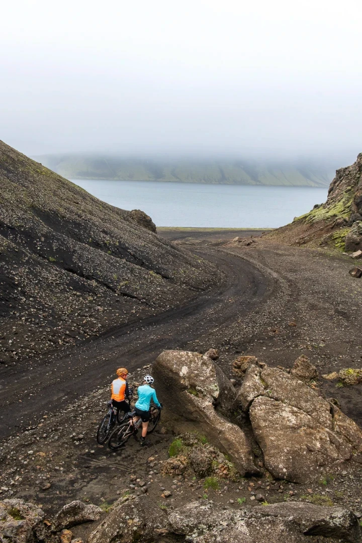 Rough gravel with two cyclists and lake in backround