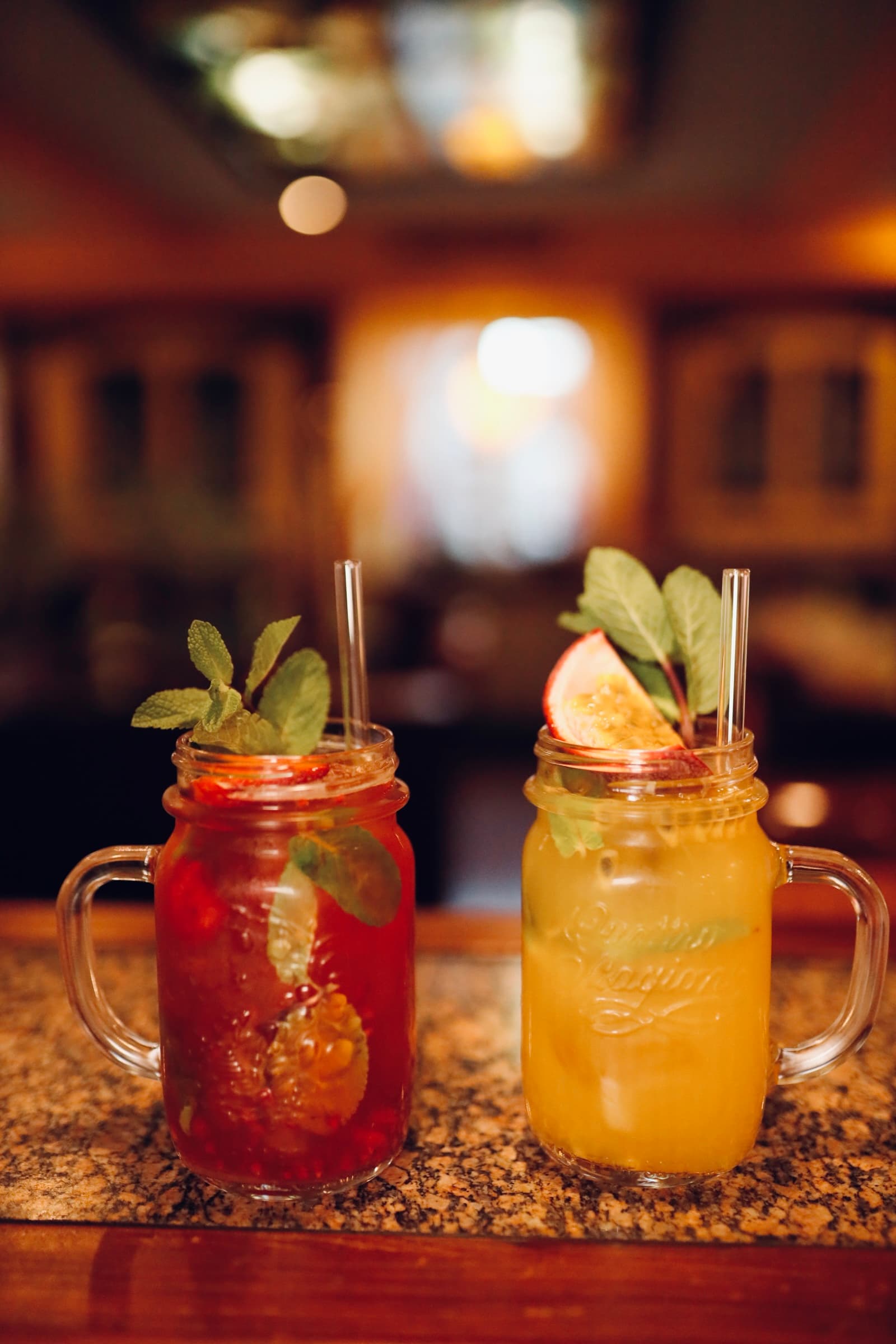 Zwei bunte Cocktails in Mason Gläsern mit Minze und Strohhalmen auf Tresen. 