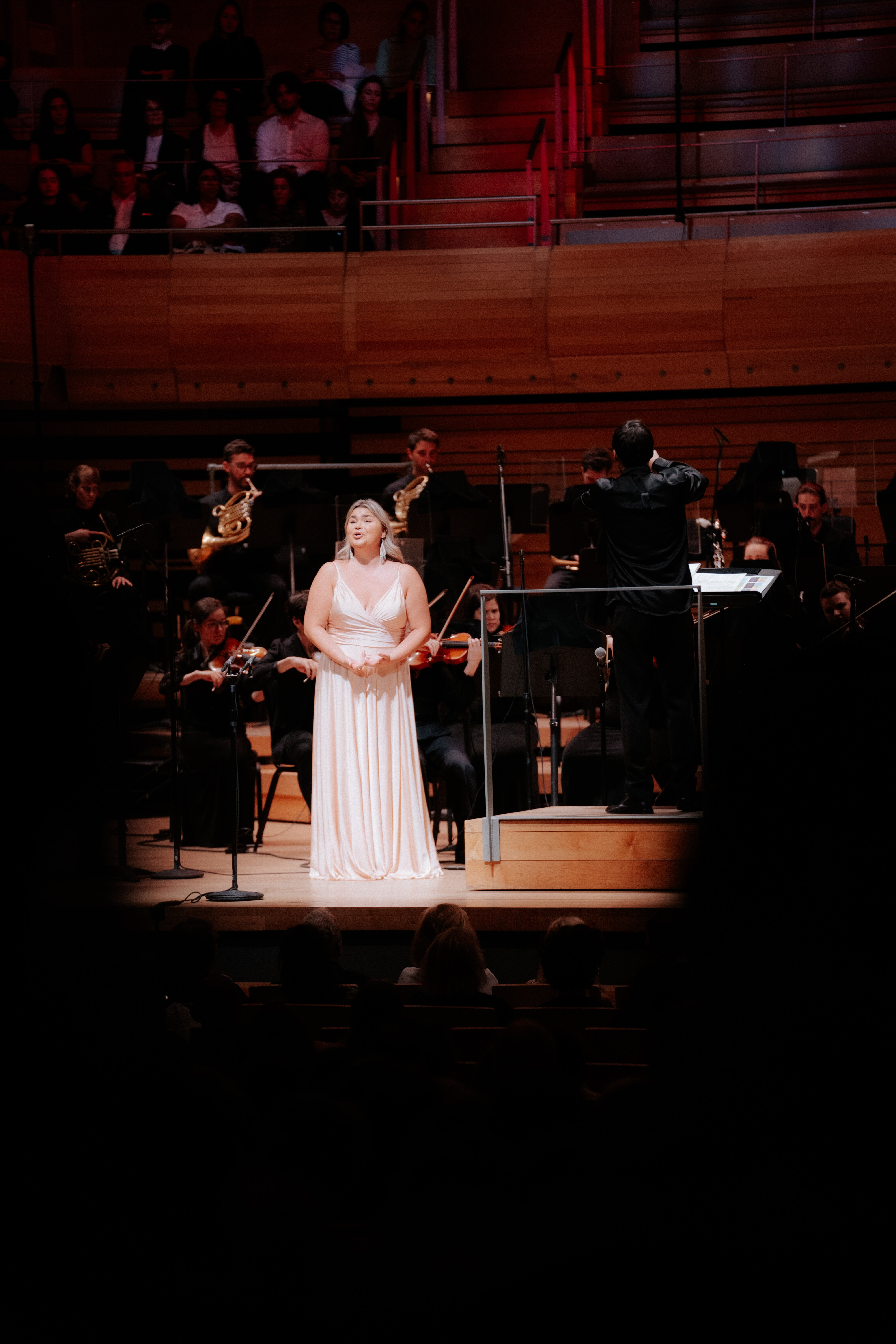Elisabeth St-Gelais interprète un solo accompagnée d’un orchestre symphonique sous la direction d’un chef d’orchestre dans une grande salle de concert.
