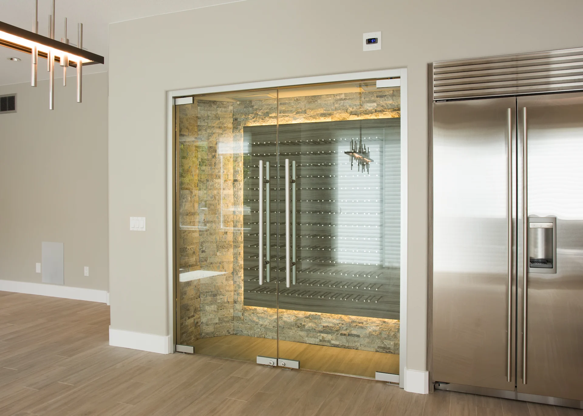 Wide view of the wine cellar doors and Sub Zero fridge, illuminated by a stylish pendant light, showcasing luxury and sophistication in the Harbor Cove remodel.