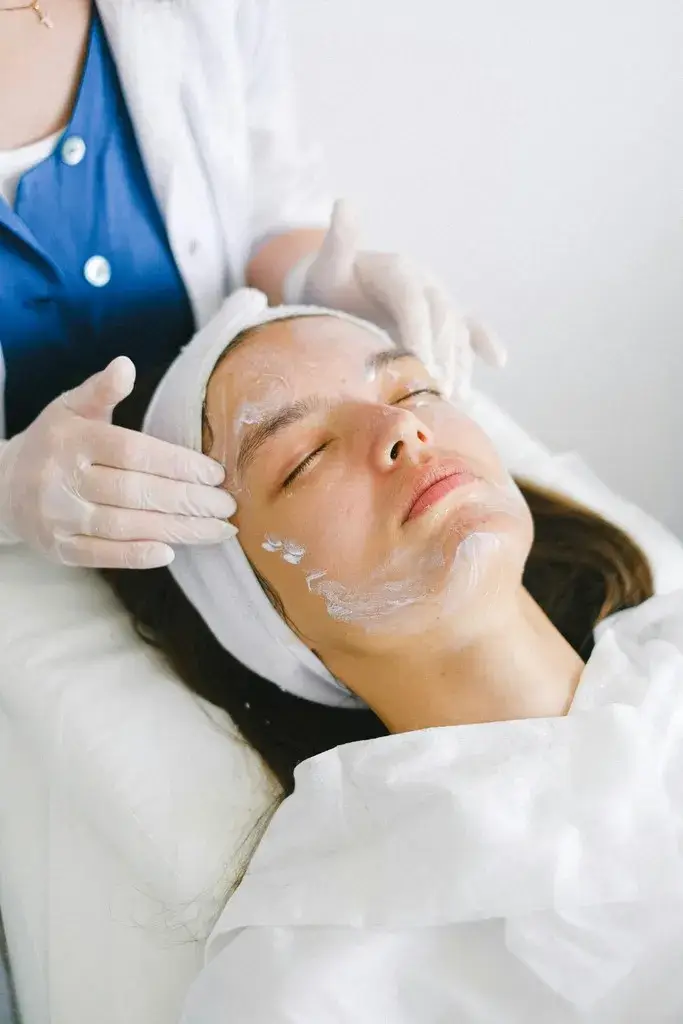 Esthetician applying facial mask treatment during a professional spa session to cleanse, exfoliate, and hydrate the skin for a smoother, brighter complexion.