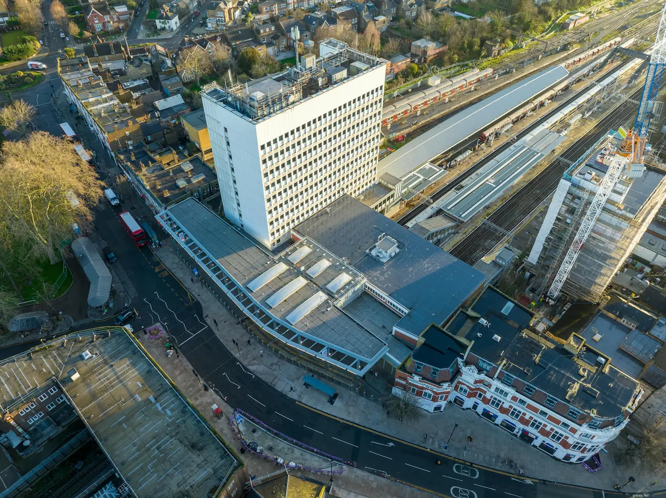 Drone photography of an urban site showing a railway station, large white building, and street layout.