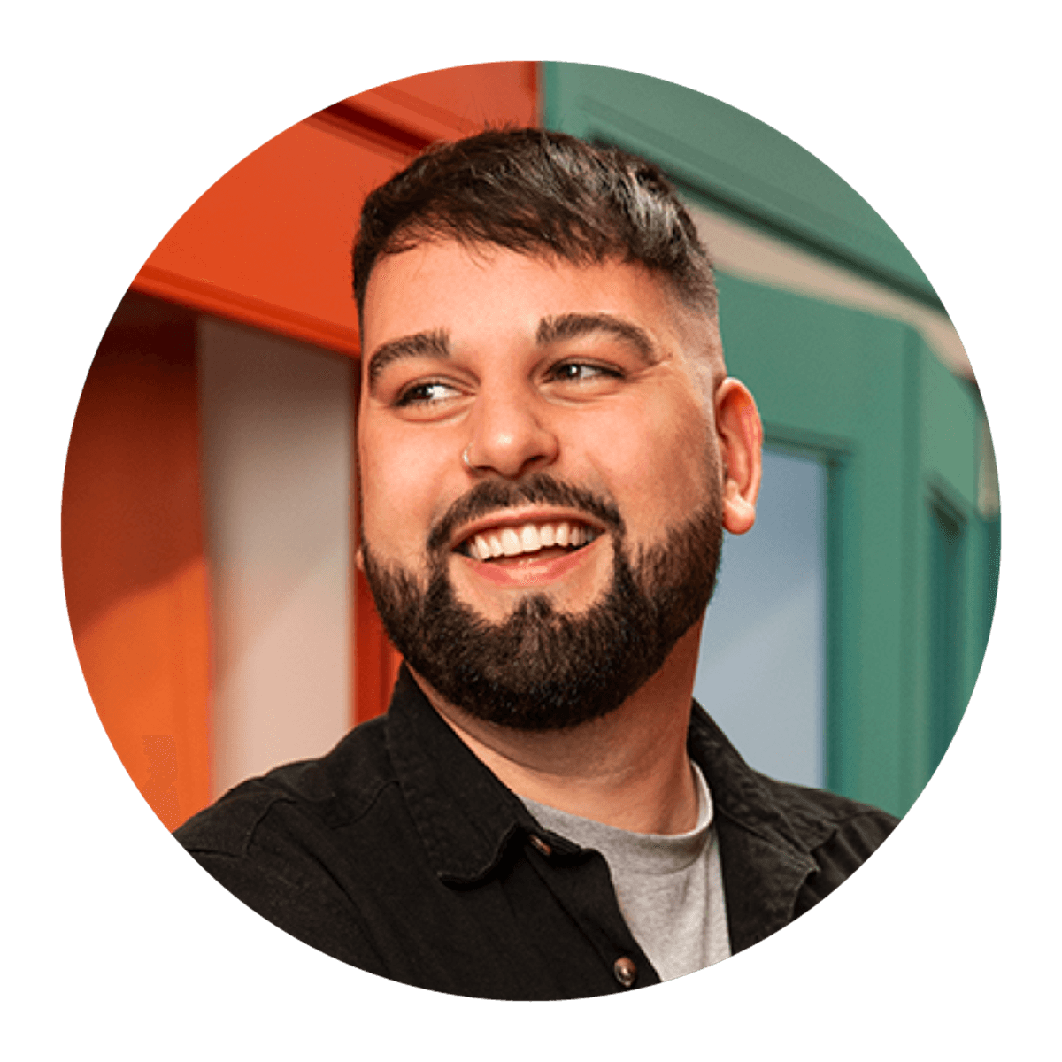 A circular portrait of a person wearing a dark jacket over a light T‑shirt, standing in front of a colorful indoor background with geometric panels.