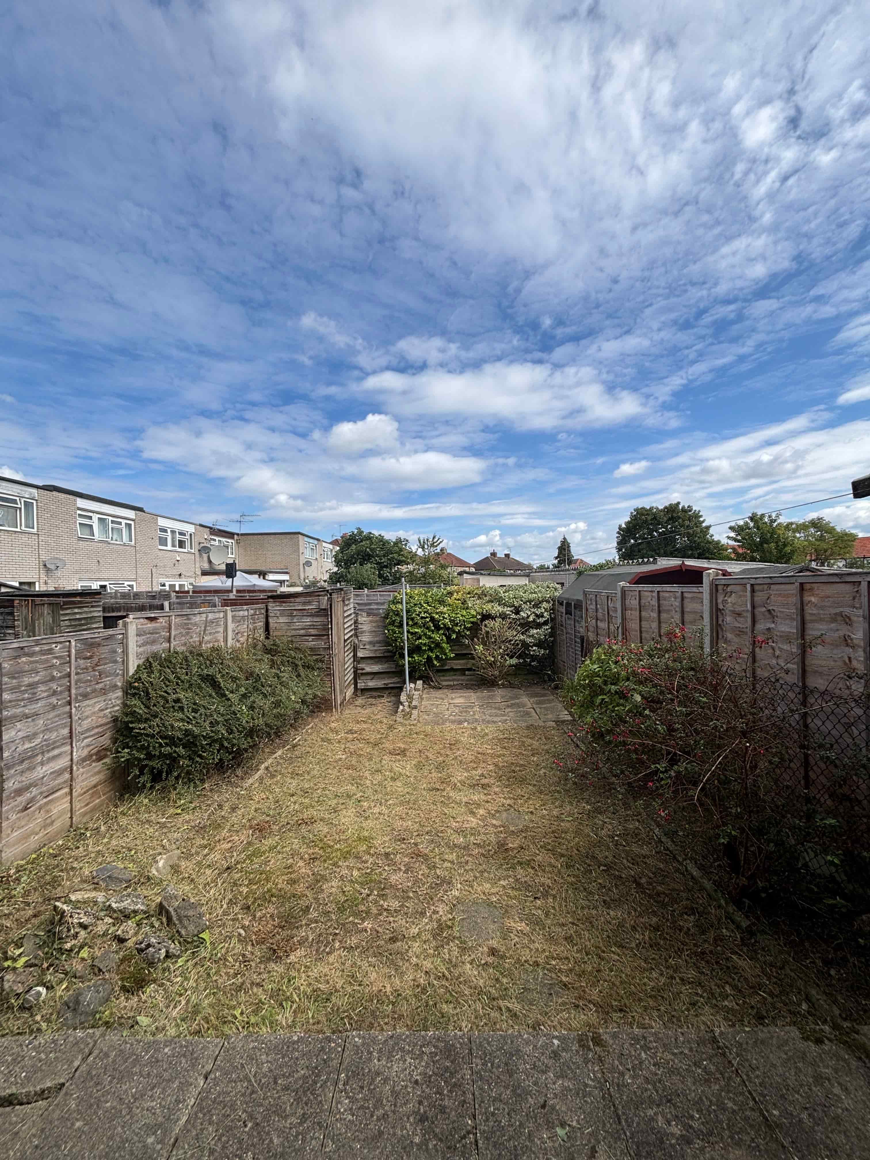 : Garden path through modern black wooden pergolas leading to a green shed.