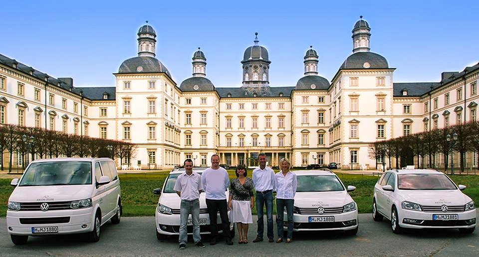 Eine Gruppe von Menschen steht vor Autos, die vor einem großen Gebäude geparkt sind.