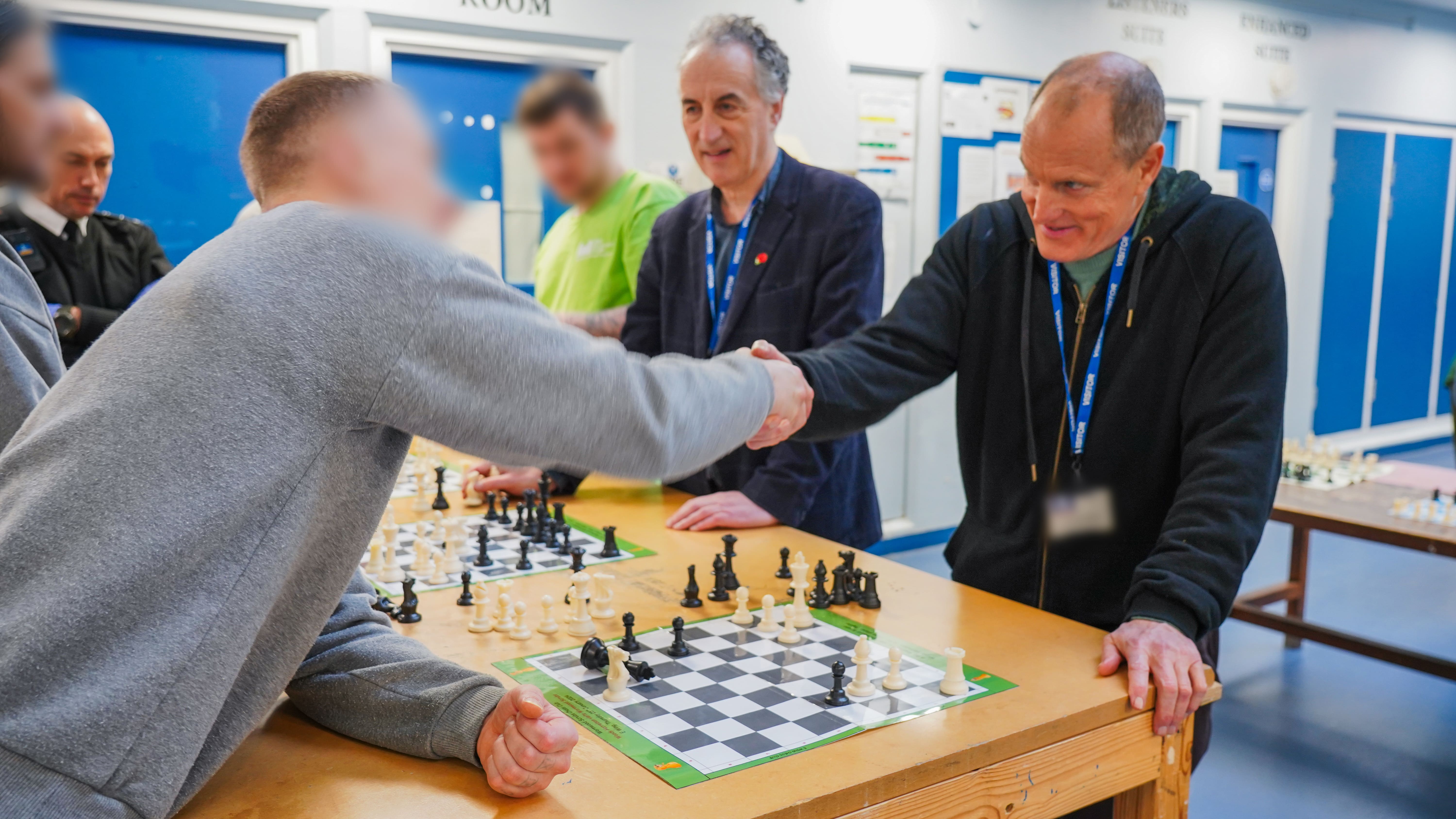 A prisoner shakes hands with actor Woody Harrelson as they finish a chess game