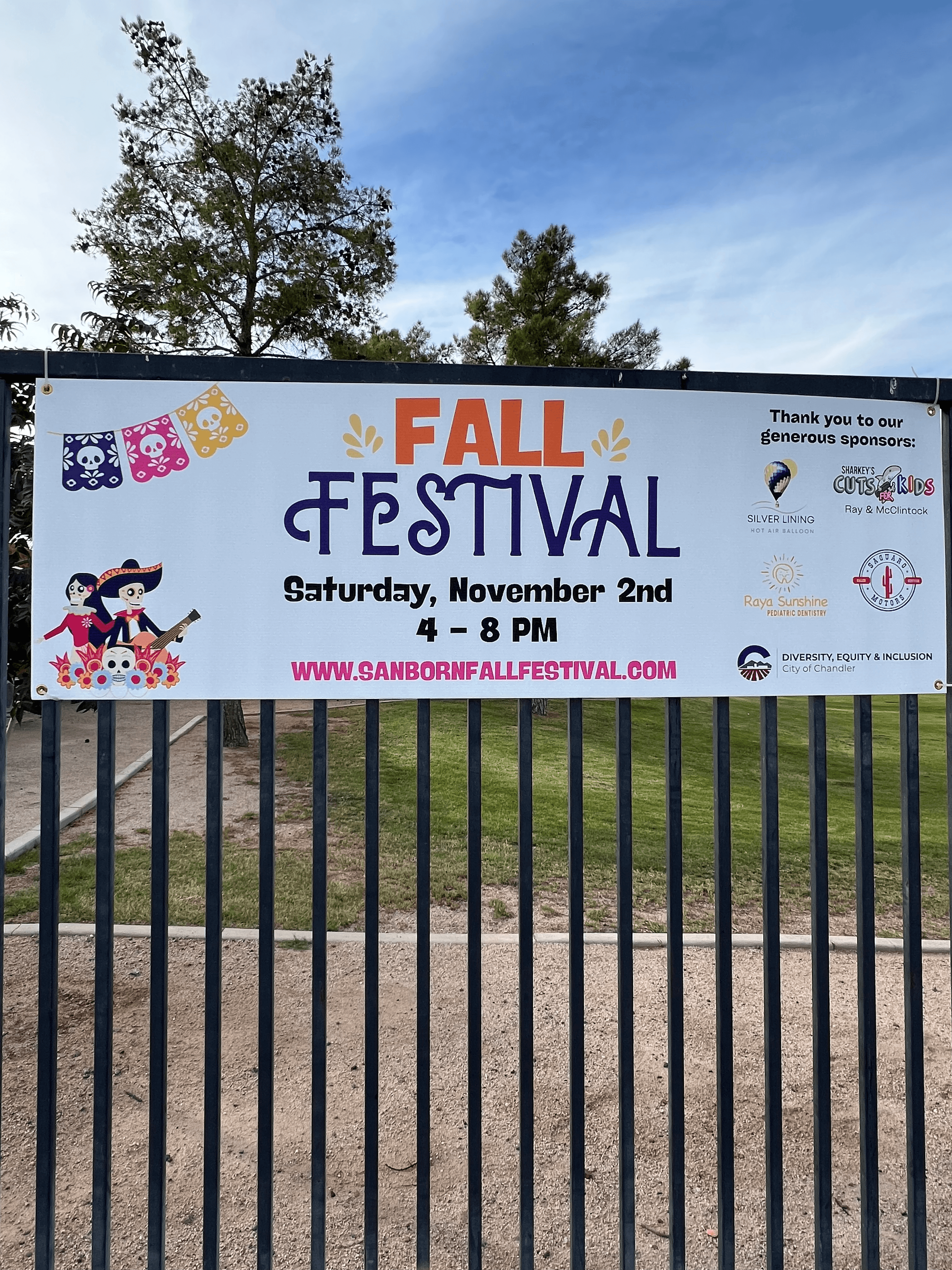 A sign on a fence reading “Fall Festival” with event details displayed outdoors
