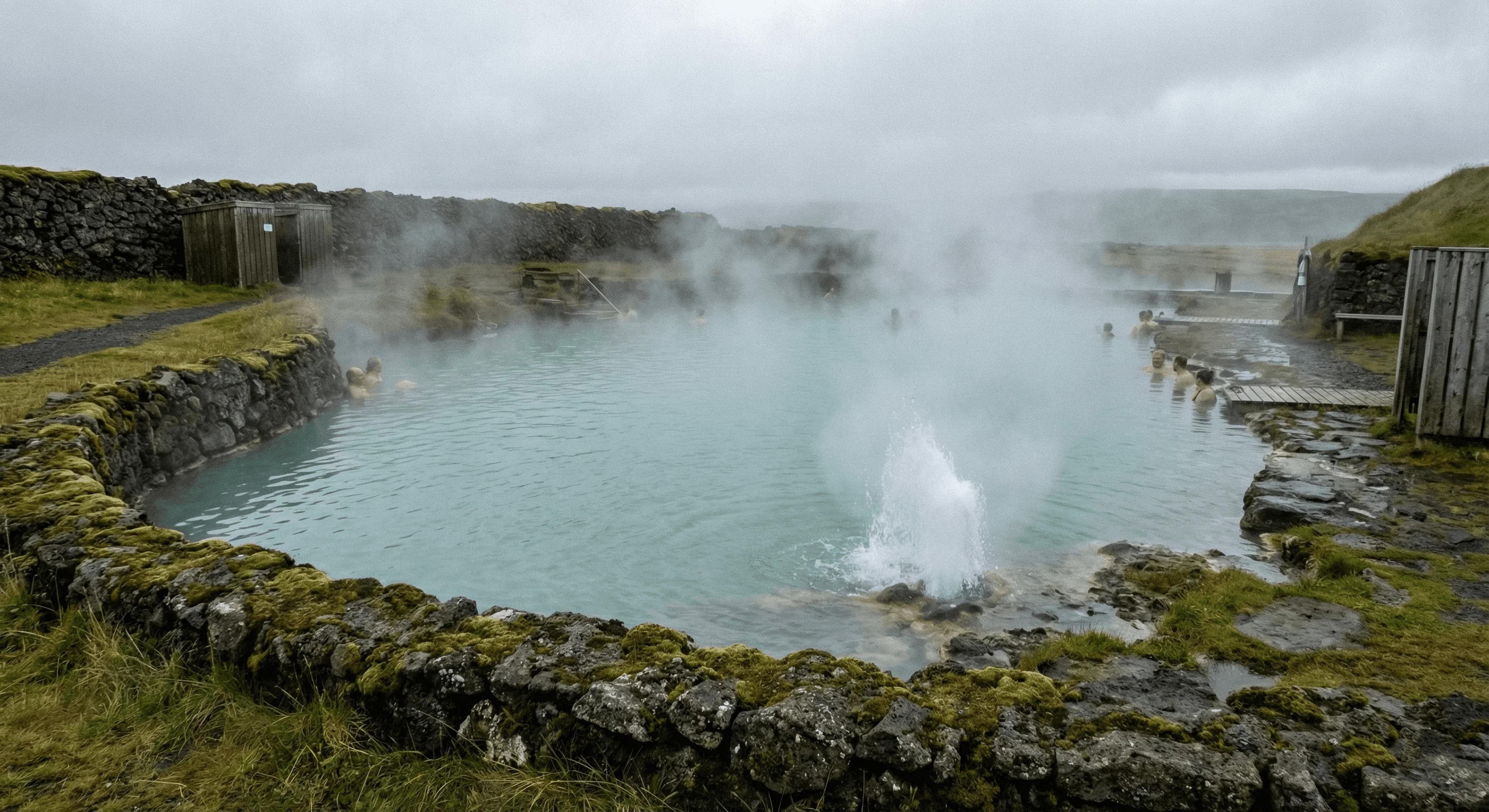 A steaming hot spring bubbling up in a geothermal area surrounded by rocks and moss.