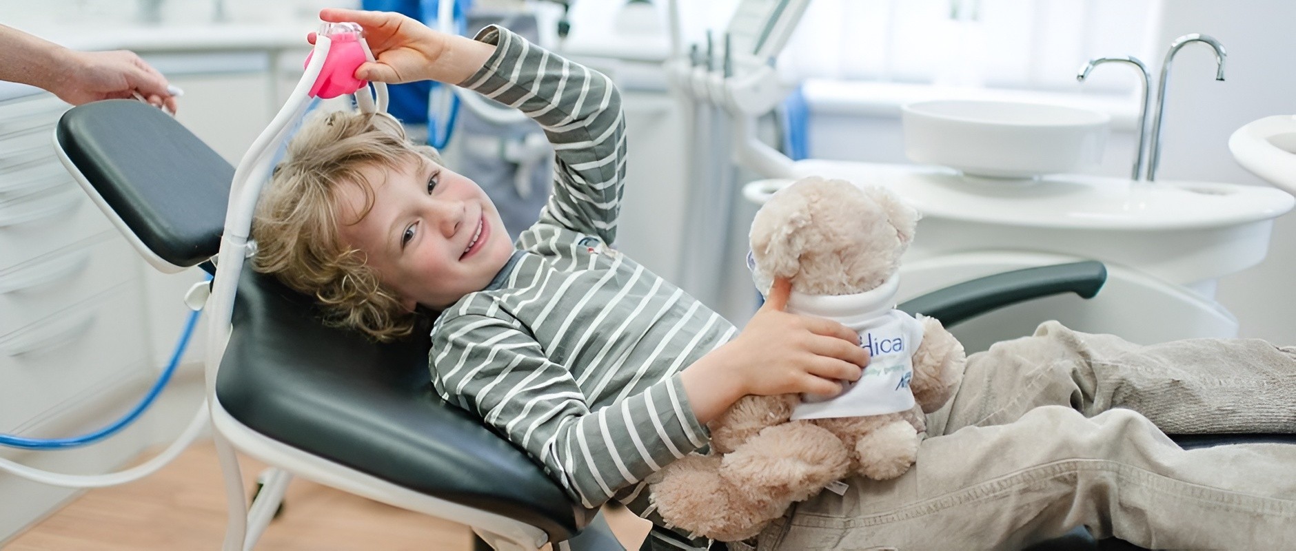 Kind beim Zahnarztstuhl hält ein Kuscheltier in einer kinderfreundlichen Praxisatmosphäre.