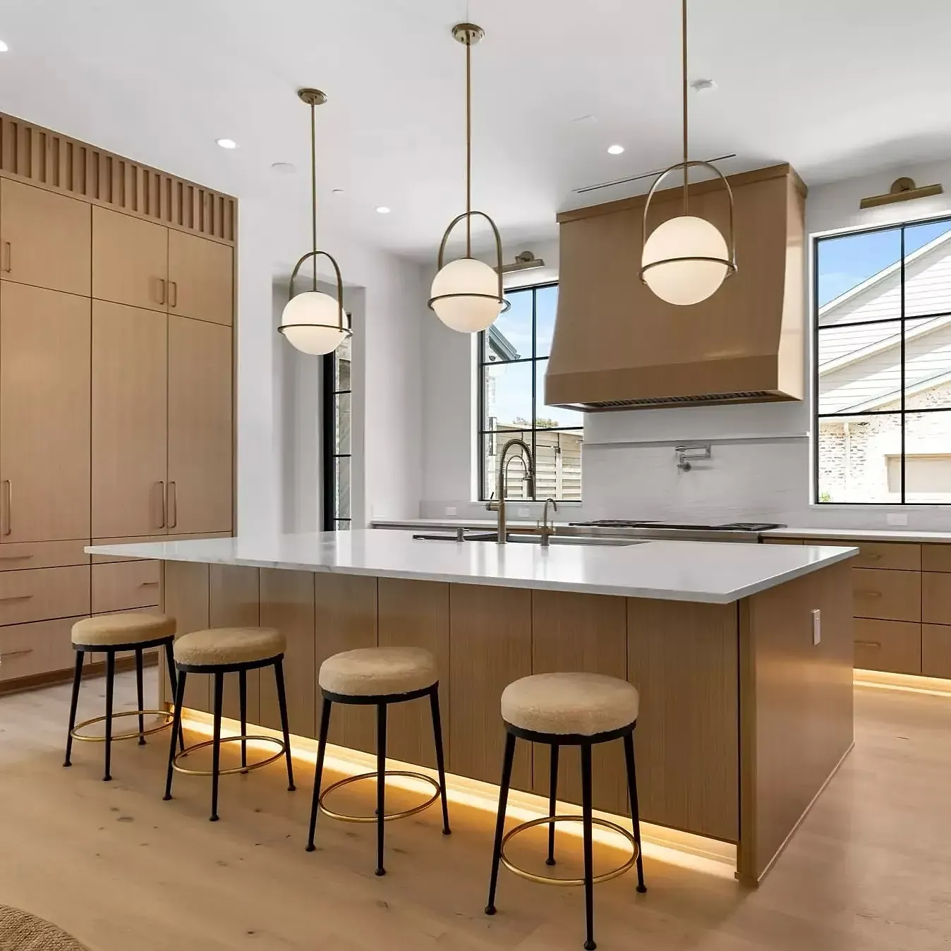 A contemporary kitchen with a long counter, stools, and pendant lights.