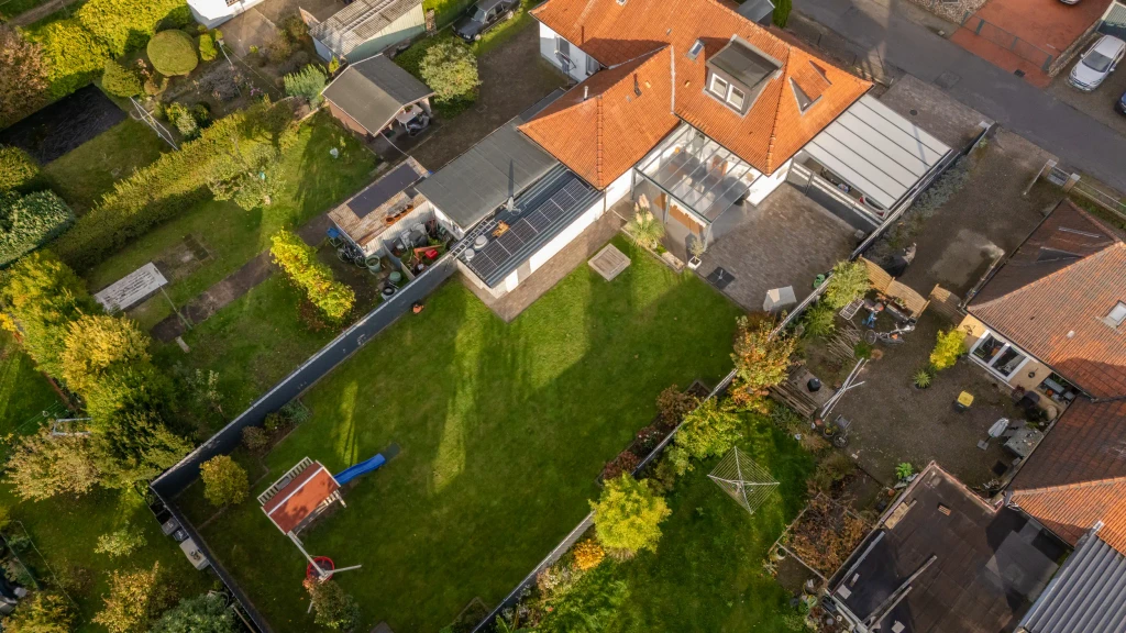 Schräg aufgenommene Drohnenansicht eines Einfamilienhauses mit Solaranlage und gepflegtem Garten in Gronau – Westfalen Wohnen.