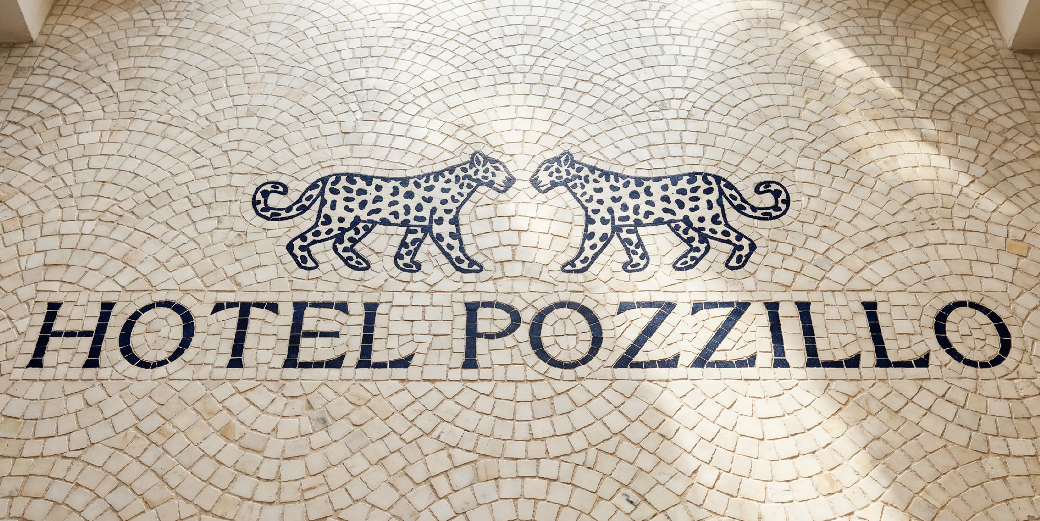 A european tiled floor with the wordmark 'Hotel Pozzillo' and the double facing leopard motifs above