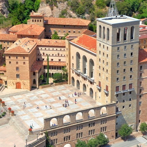 Aerial view of a historic courtyard with people walking, surrounded by multi-story buildings with red-tiled roofs.