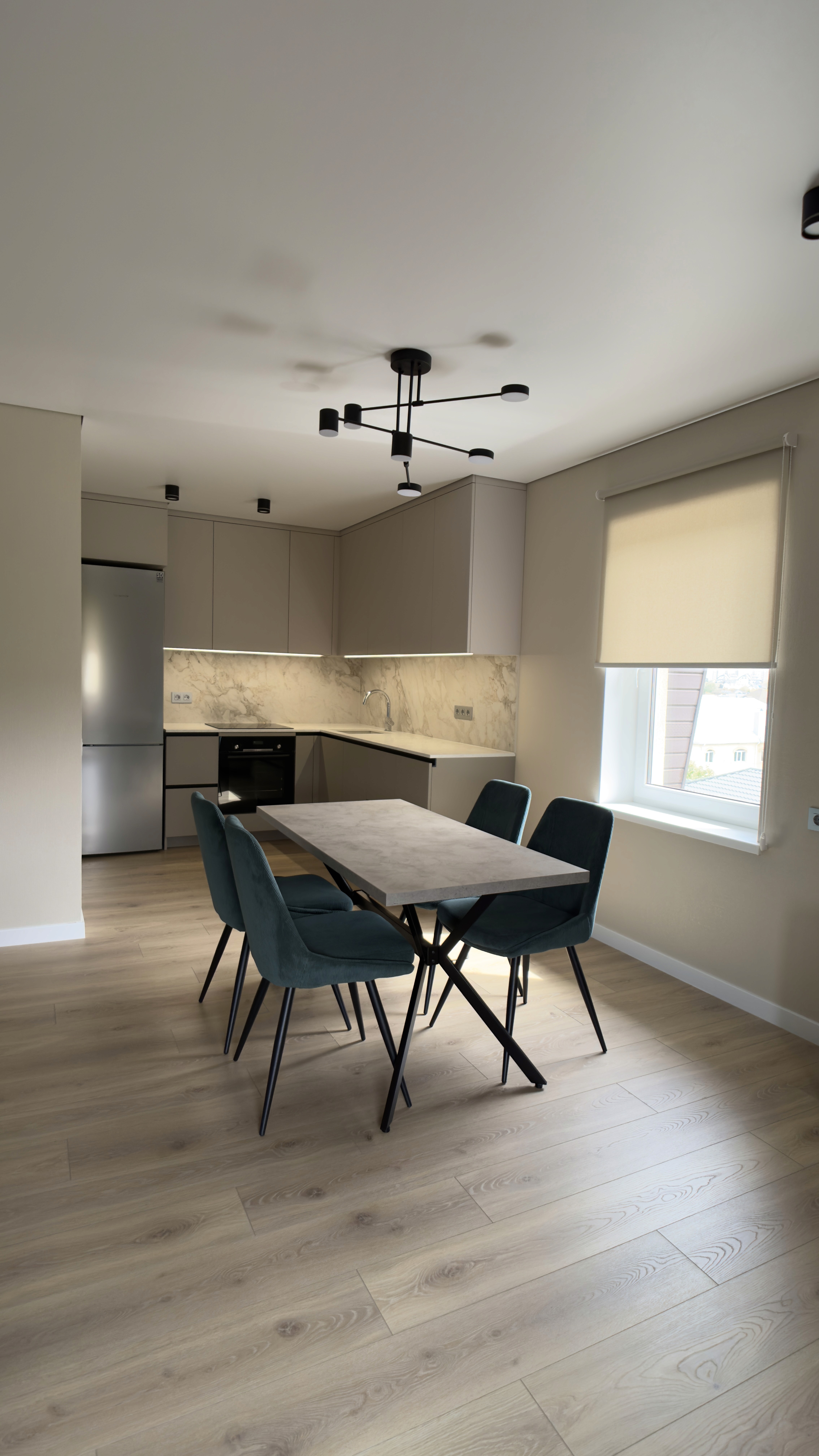 Кухня-студія з обіднім столом і смарагдовими стільцями біля вікна