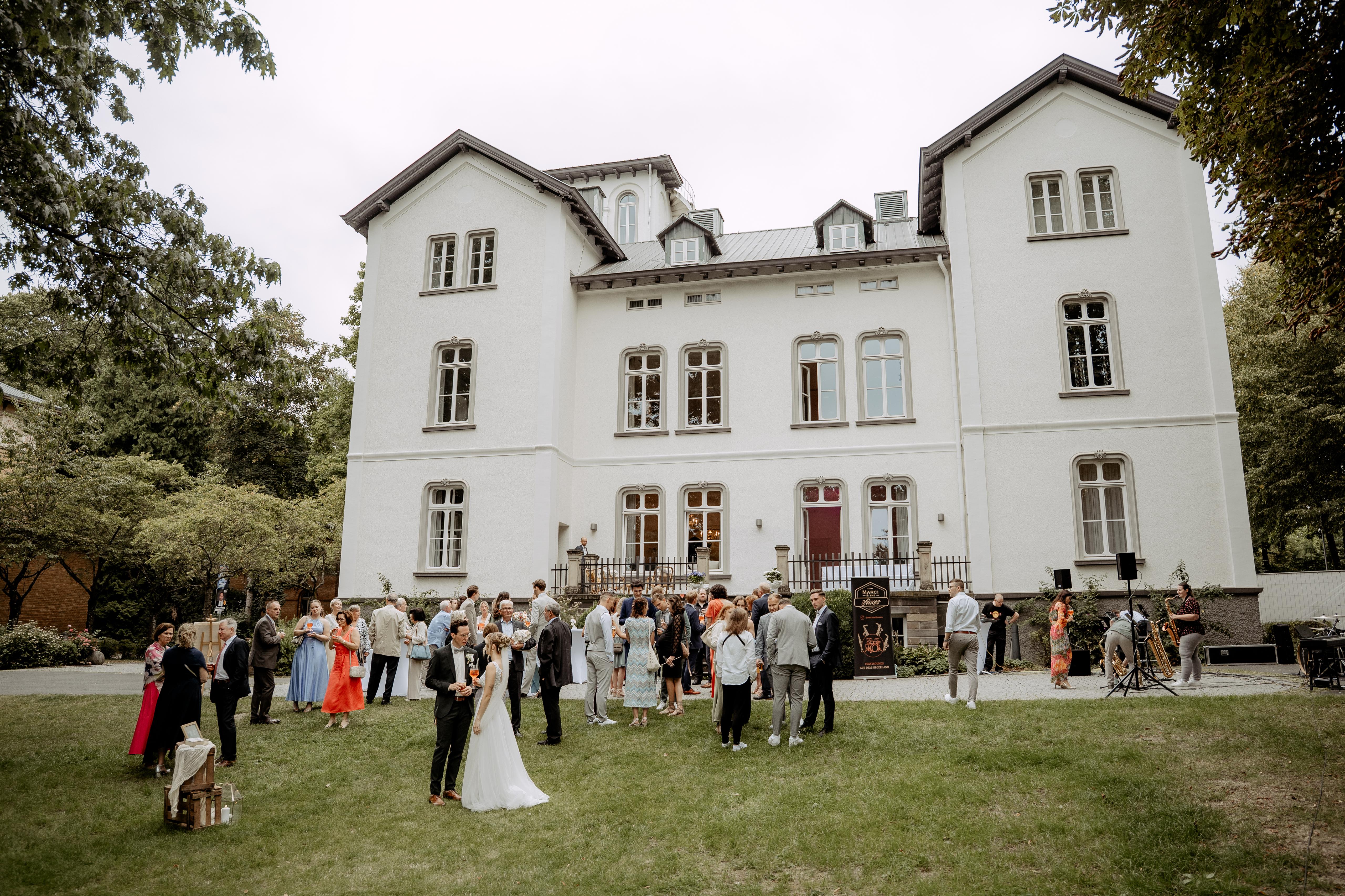 Braut im eleganten Kleid öffnet Fenster mit Blick ins Grüne