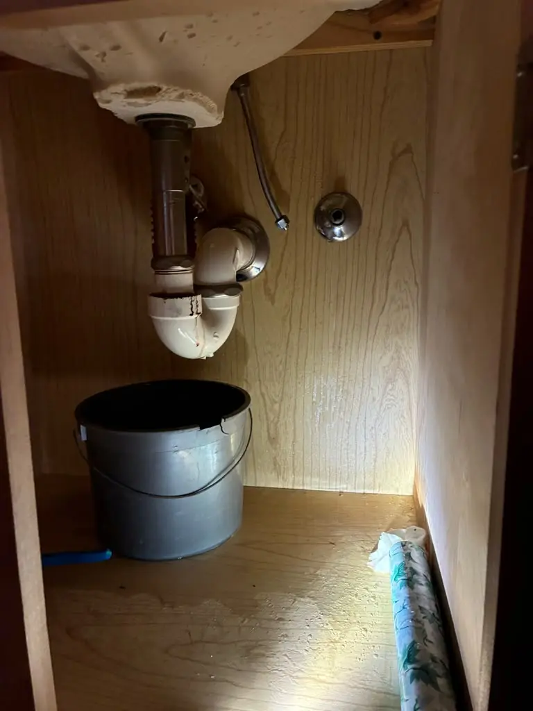 A bucket catching water from a leaking bathroom sink drain, representing the 24/7 emergency plumbing services we offer alongside our sump pump repairs.
