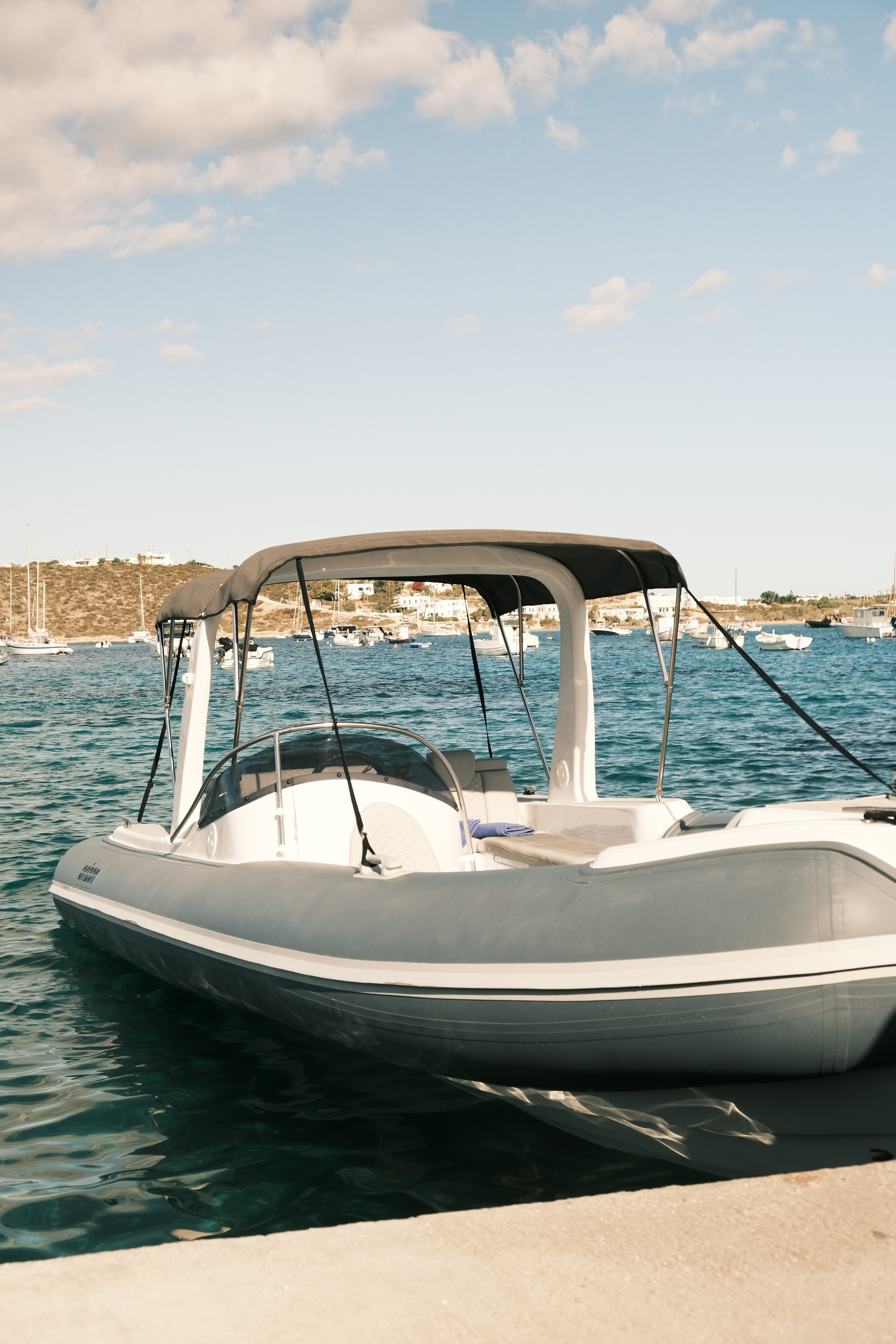 White Orizon inflatable speedboat moored in a Greek harbor with traditional fishing boats and Cycladic buildings in the background.