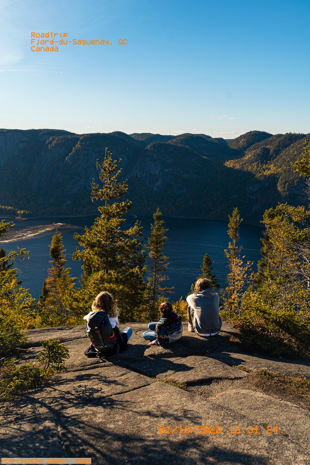 Trois randonneurs assis face au fjord et aux montagnes à perte de vue.