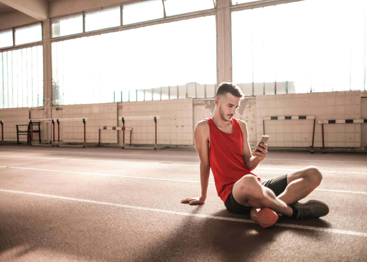 Man sitting in an indoor running track while staring at phone