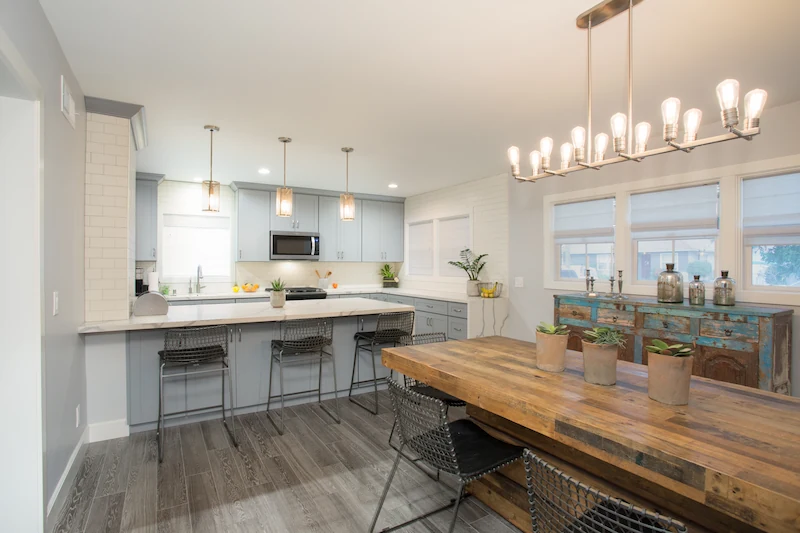 Rustic farmhouse dining room with kitchen in background. Grey floors and blue cabinetry. Photo by Chris Darnall.