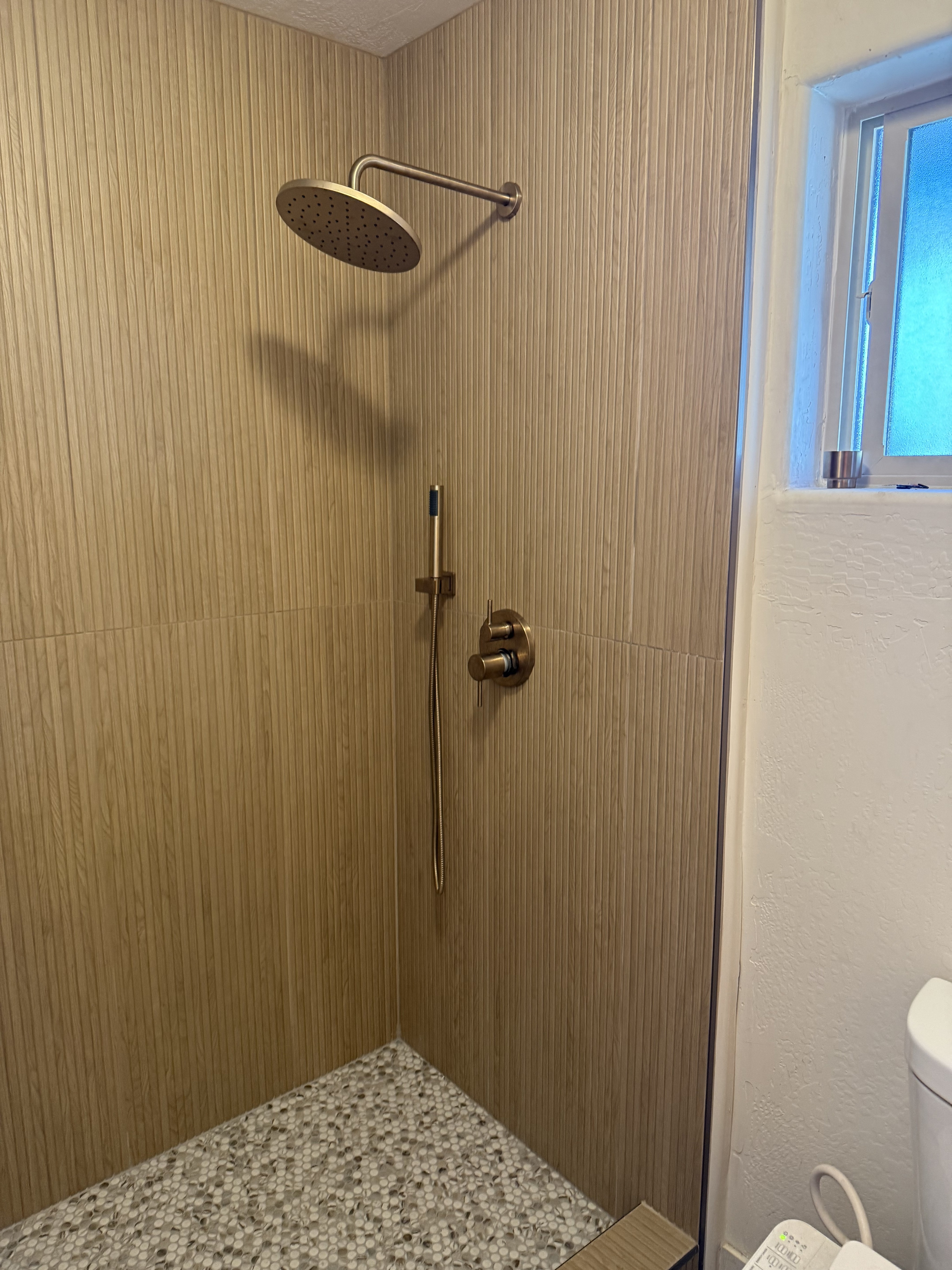 Close-up of a shower niche featuring a vibrant blue and black shattered glass or pebble mosaic tile insert, framed by light beige natural stone wall tiles.