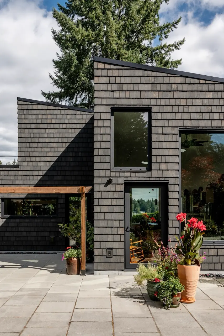 Modern two-story home with large glass windows, warmly lit interiors, and a balcony. Surrounded by trees and a manicured lawn at dusk. Cozy ambiance.