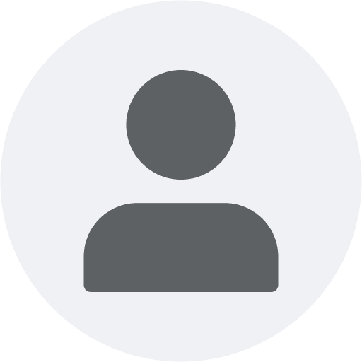 Portrait of a woman with pulled-back hair, wearing a textured sweater, seated in warm natural light against a soft brown background.