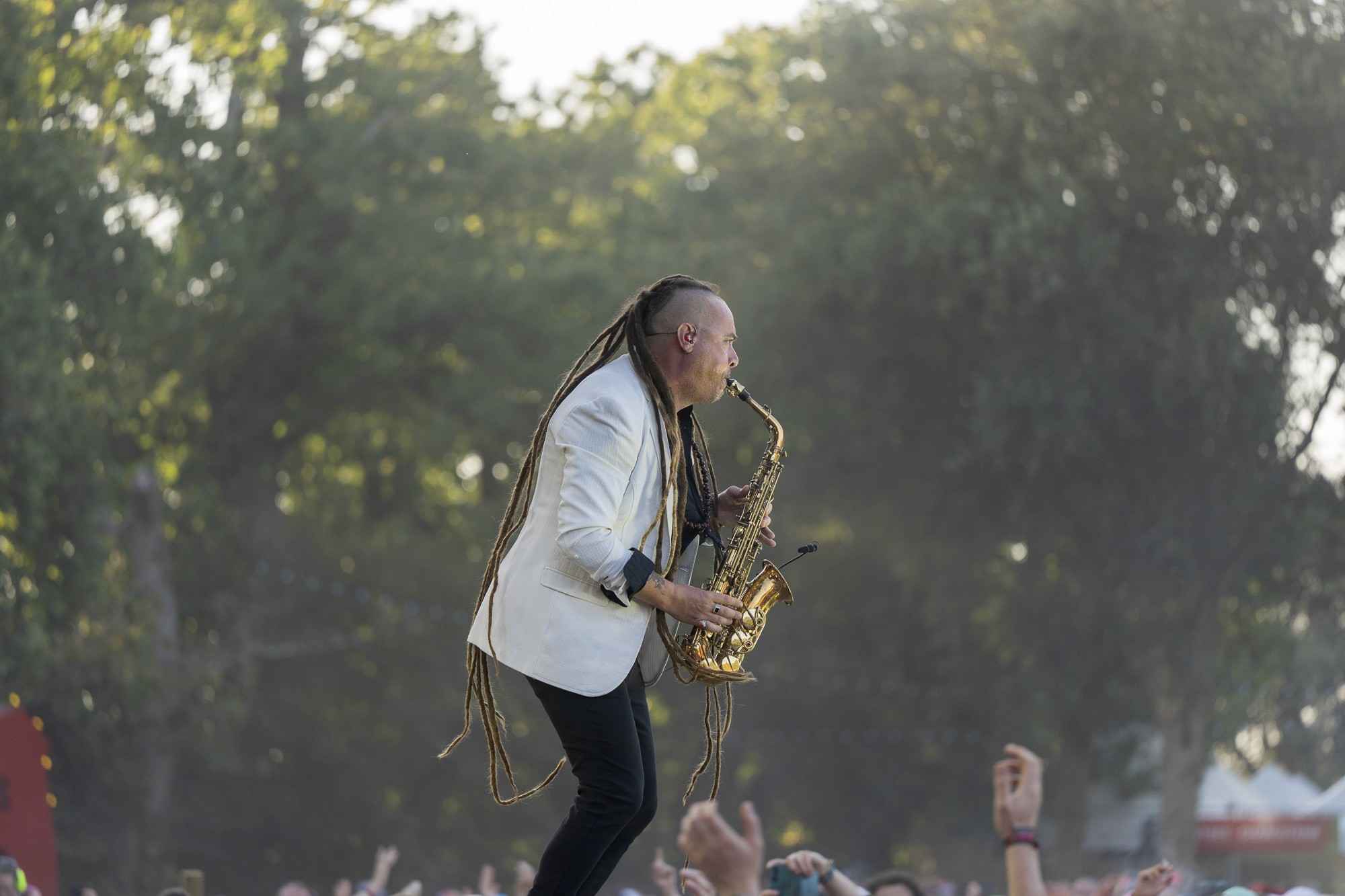 Saxophoniste en veste blanche jouant au-dessus de la foule, lumière du soir dans les arbres
