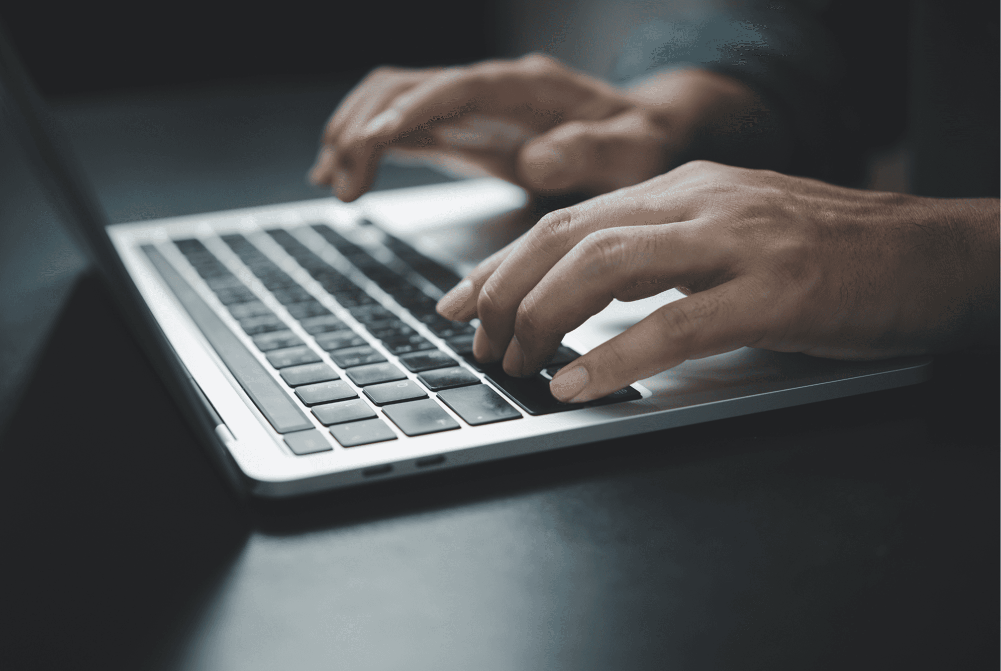 Mãos digitando em teclado de notebook sobre mesa, com xícara branca ao lado