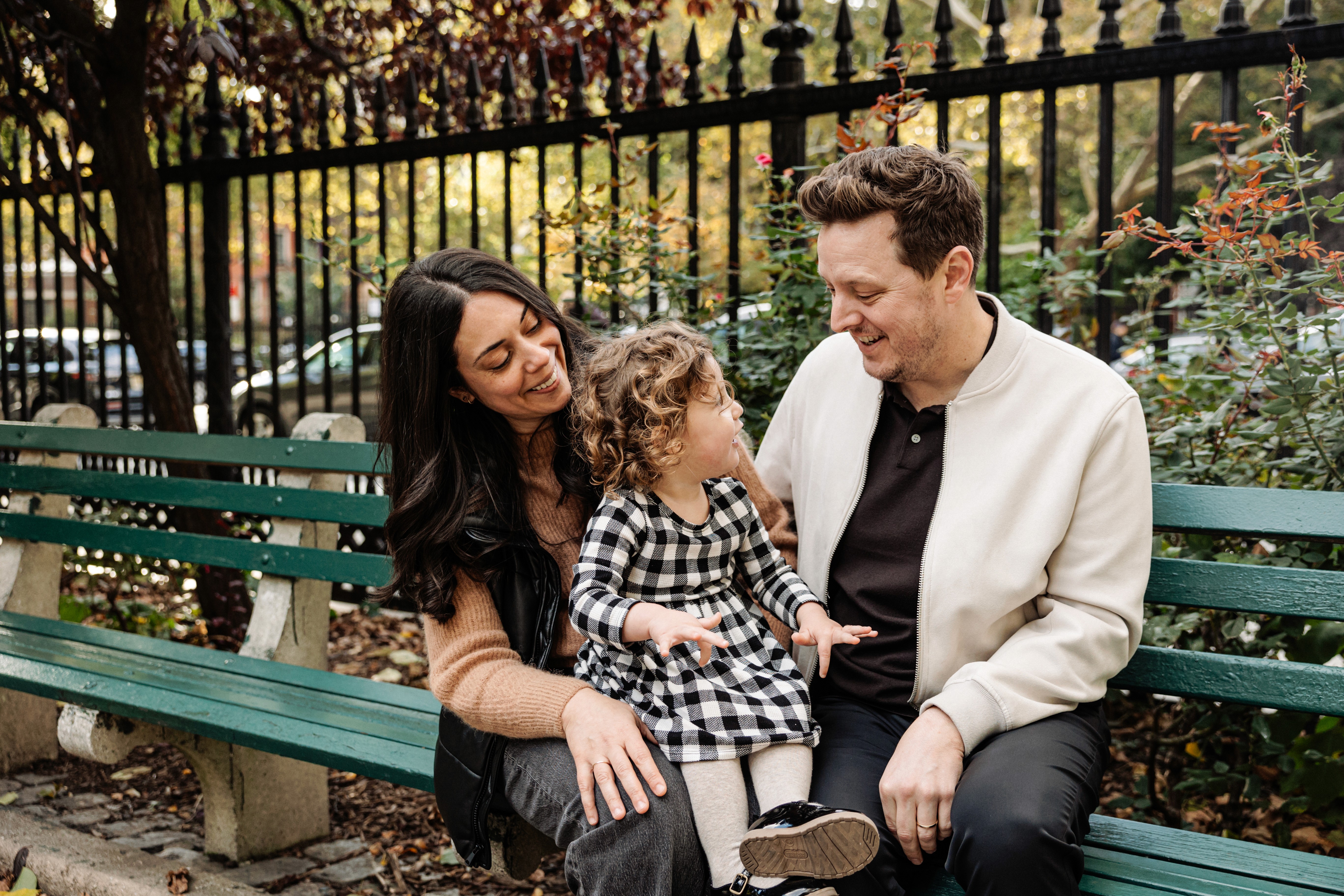 Mom holding her daughter close while dad stands proudly by their side at Stuyvesant Square Park in the Gramercy and East Village neighborhood of NYC — warm, candid family photography by Lizz Spano Photography, New York City family photographer.