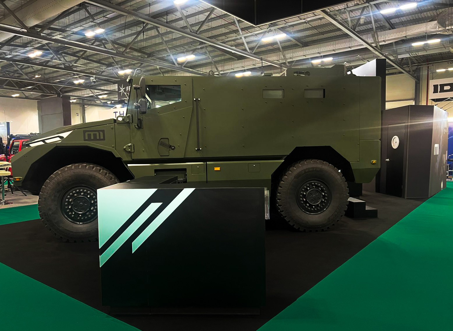 Stand INKAS Armored Farnborough 2026 par Expace – vue d'ensemble avec véhicules blindés et maquettes défense sur comptoirs noirs, identité militaire vert et noir