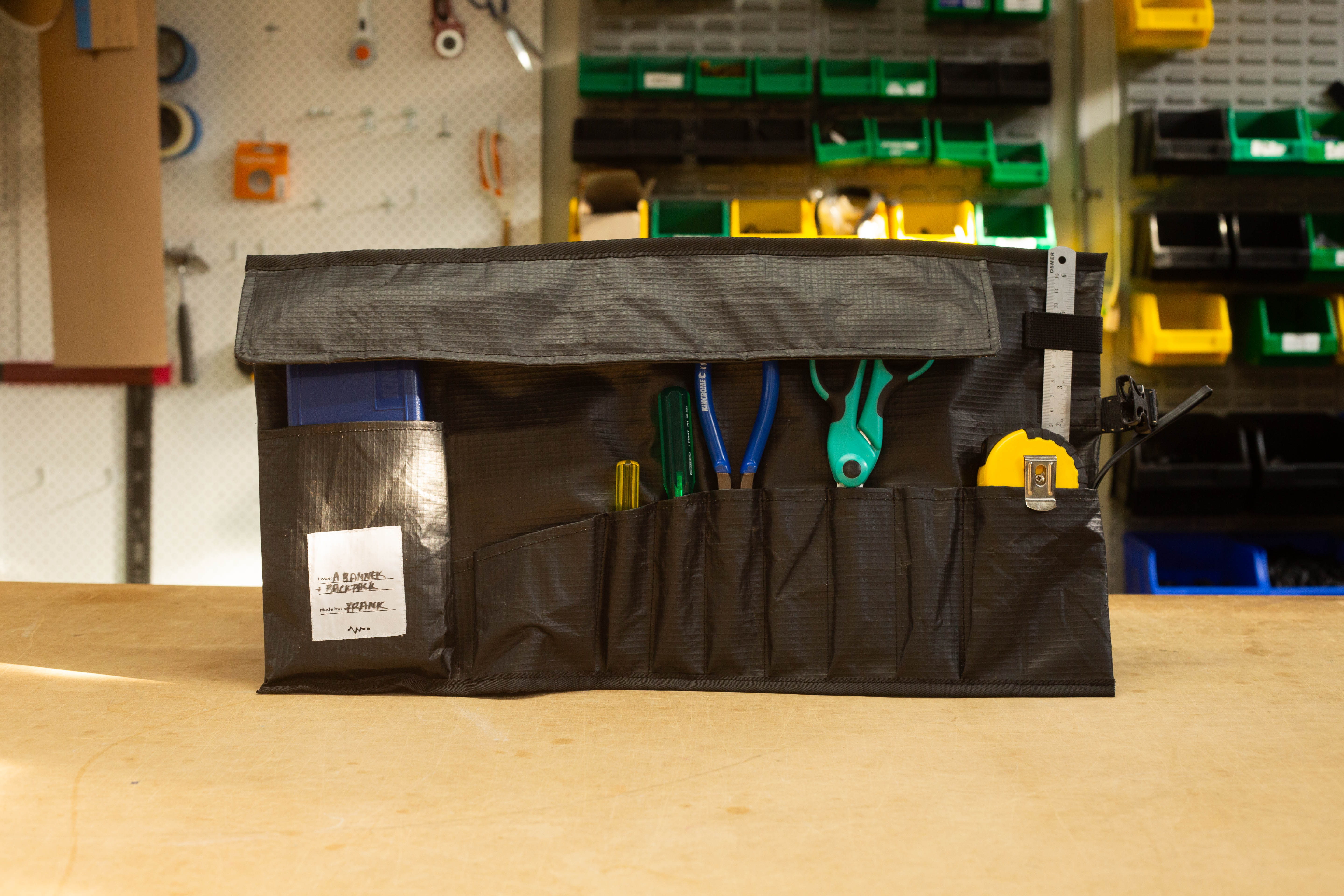 Upcycled tool roll made from black outdoor advertising banner, displaying neatly organized hand tools.