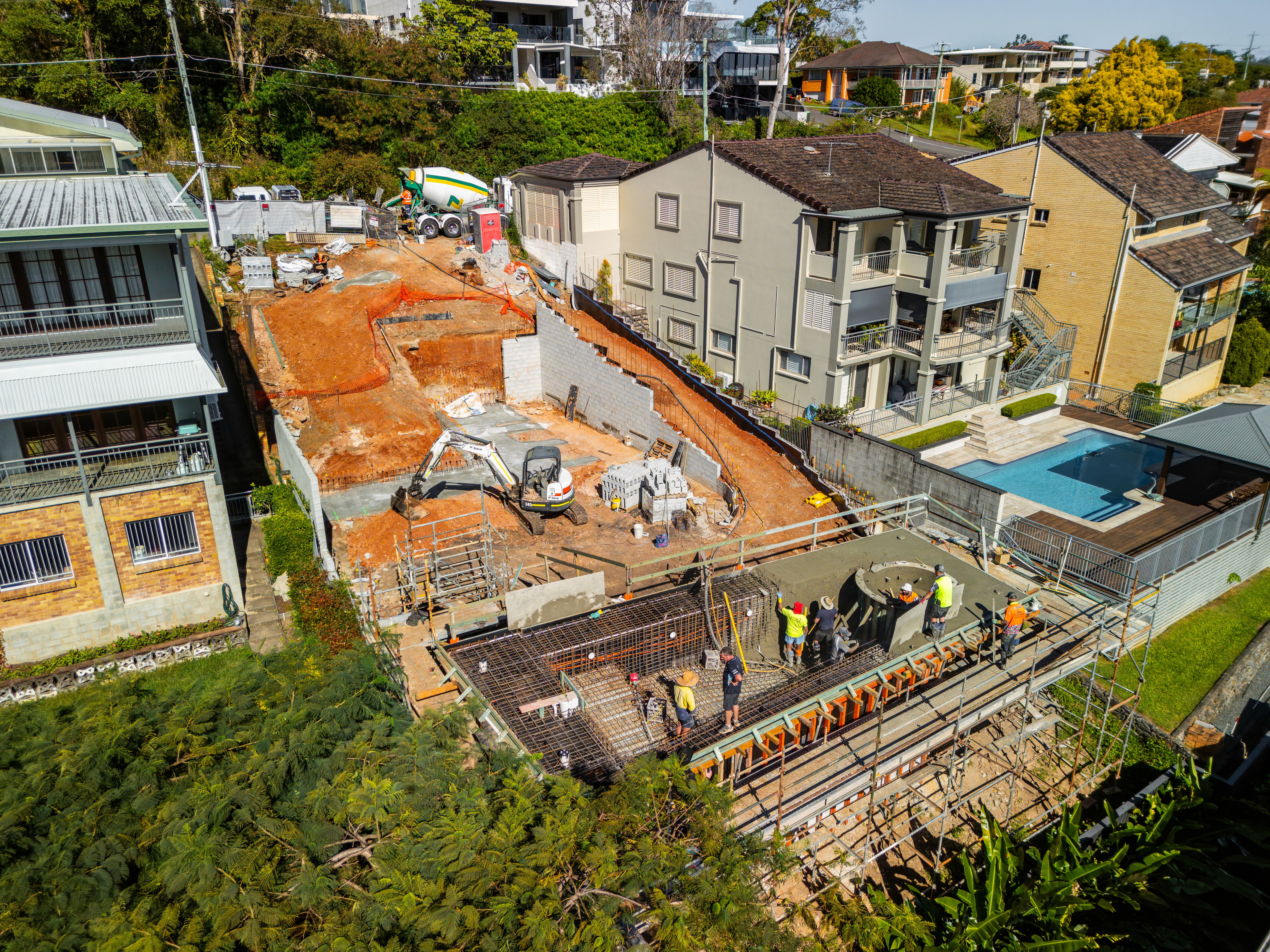 Aerial construction view by Flascon Construction Group showing complex engineering, retaining walls, and stepped slab preparation on a steep sloping block in Brisbane.