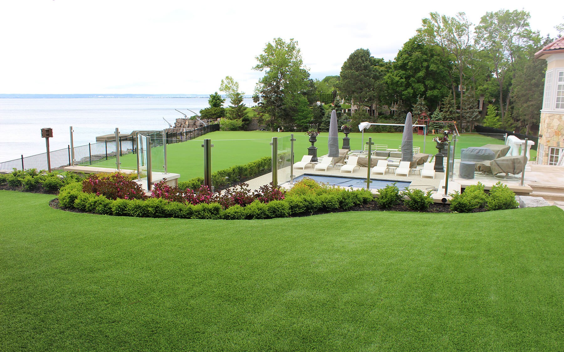 A lush artificial AGL Grass lawn blending nature with home life in a bright, sunny environment near the water.