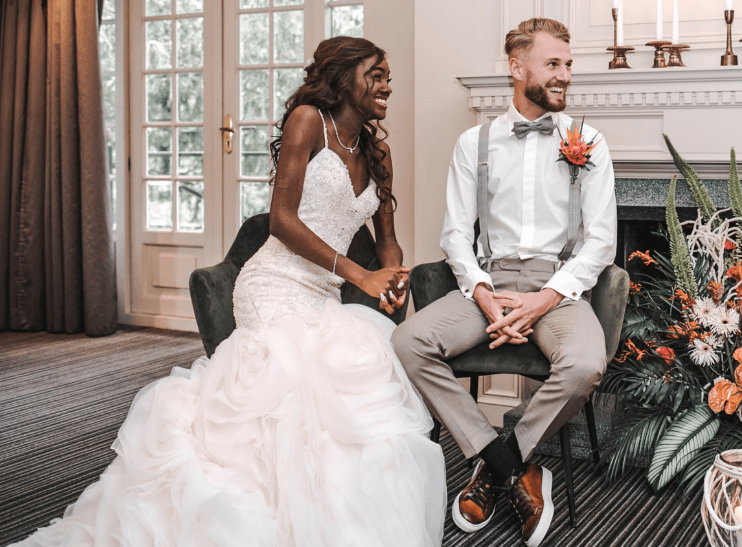 Een stralend bruidspaar zit hand in hand tijdens hun huwelijksceremonie, omringd door bloemen en sfeervolle decoratie — een liefdevolle trouwdag vol trouwinspiratie.