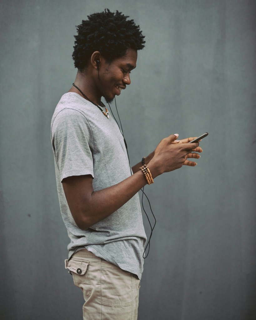 A person with curly hair stands sideways, focused on their phone, against a plain background.