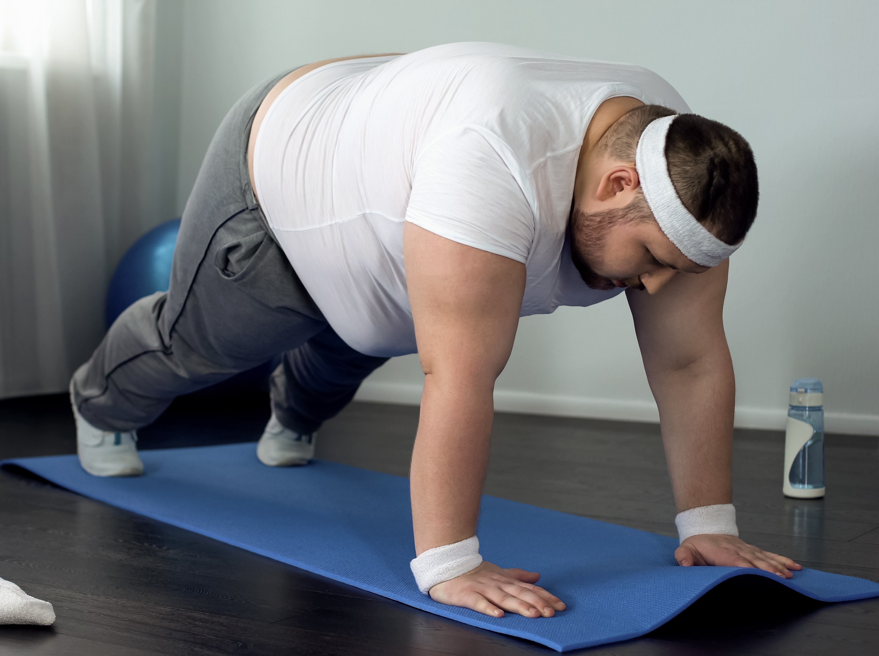overweight man doing pushups during a beginner workout for weight loss at home in his apartment