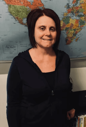 A young person with long, wavy hair sits in front of a plain background, looking directly at the camera.