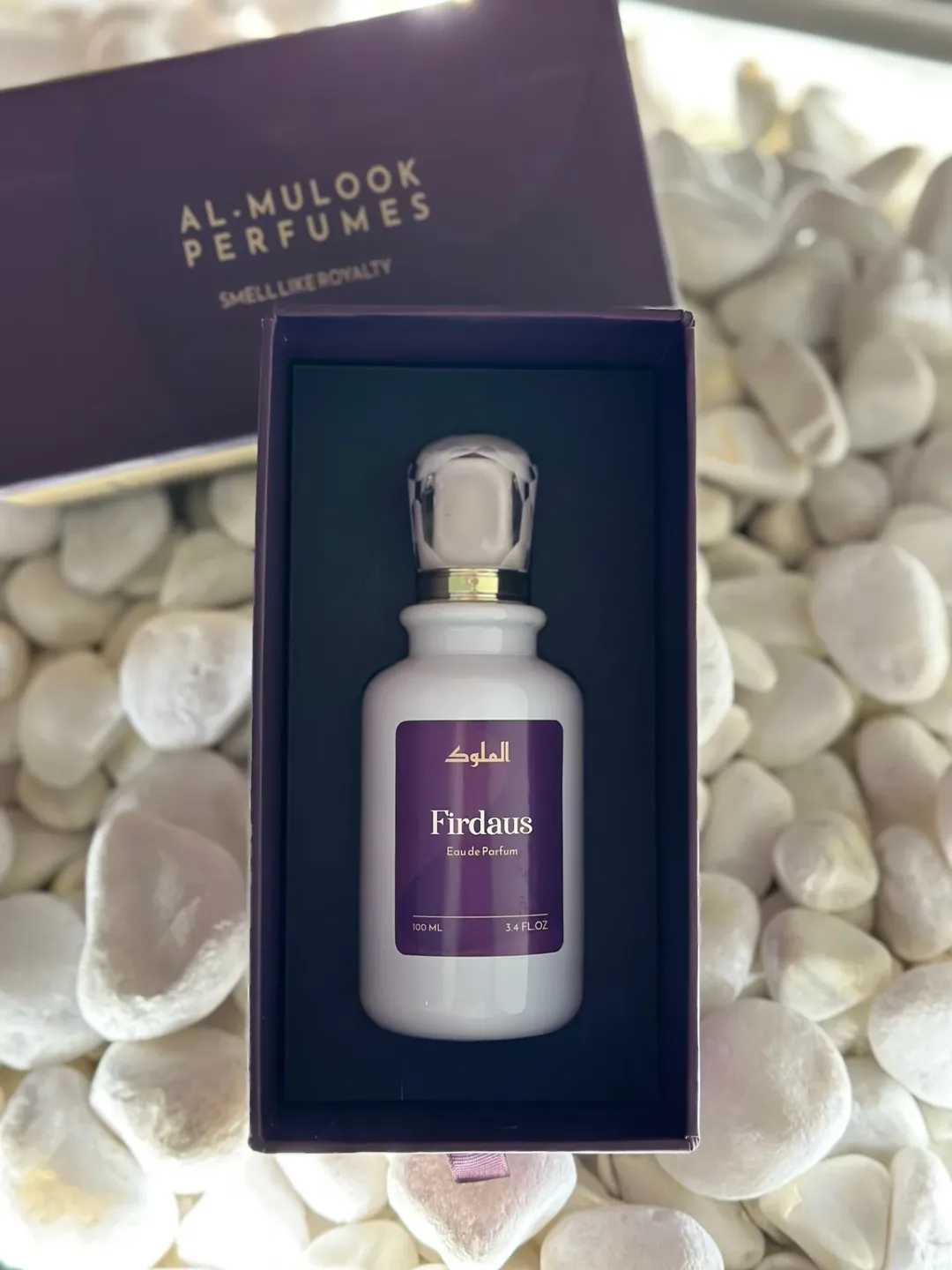 Al-Mulook perfume bottle styled among white stones with soft lighting.